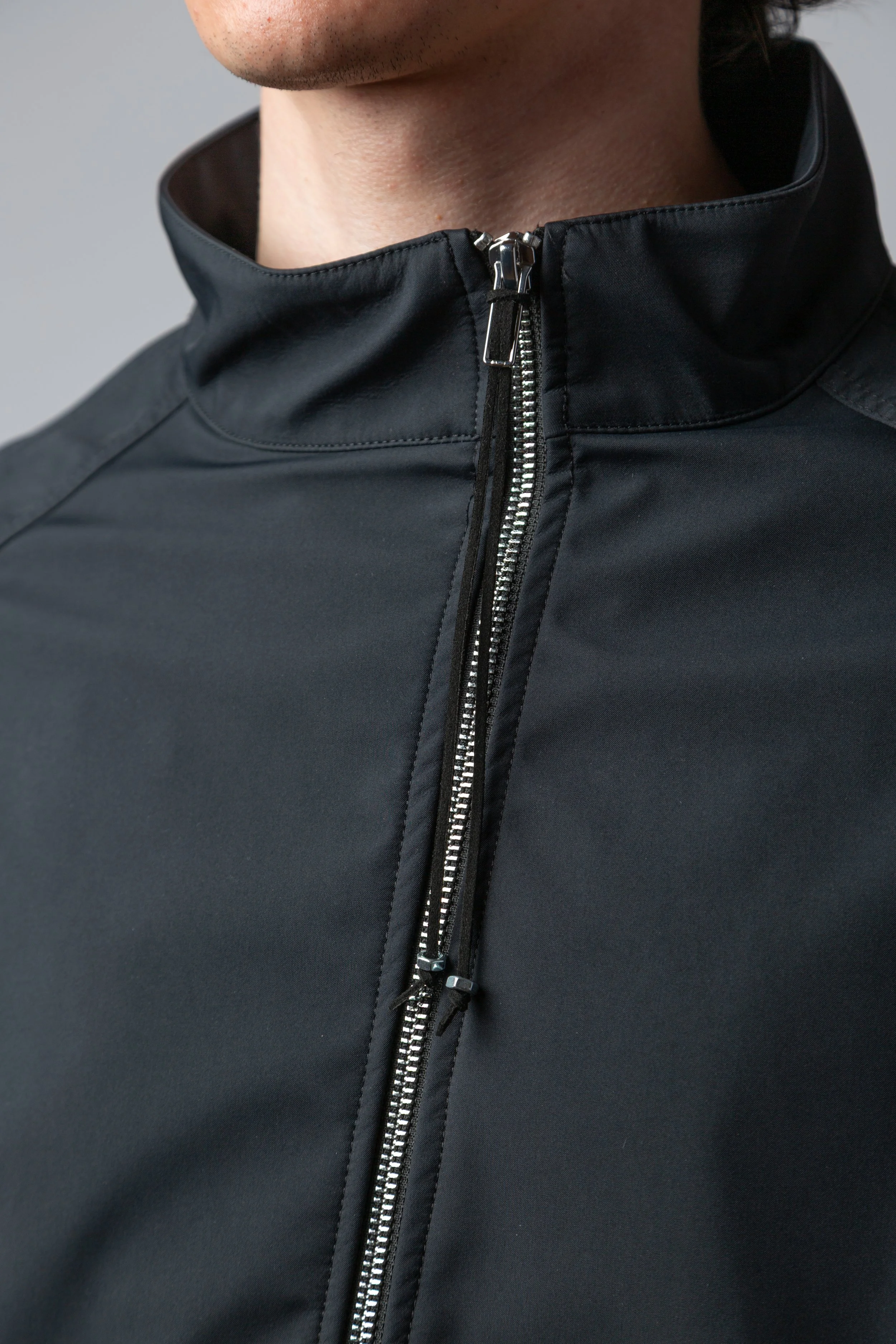 Close-up of a person wearing a black high-collared jacket with a silver zipper.