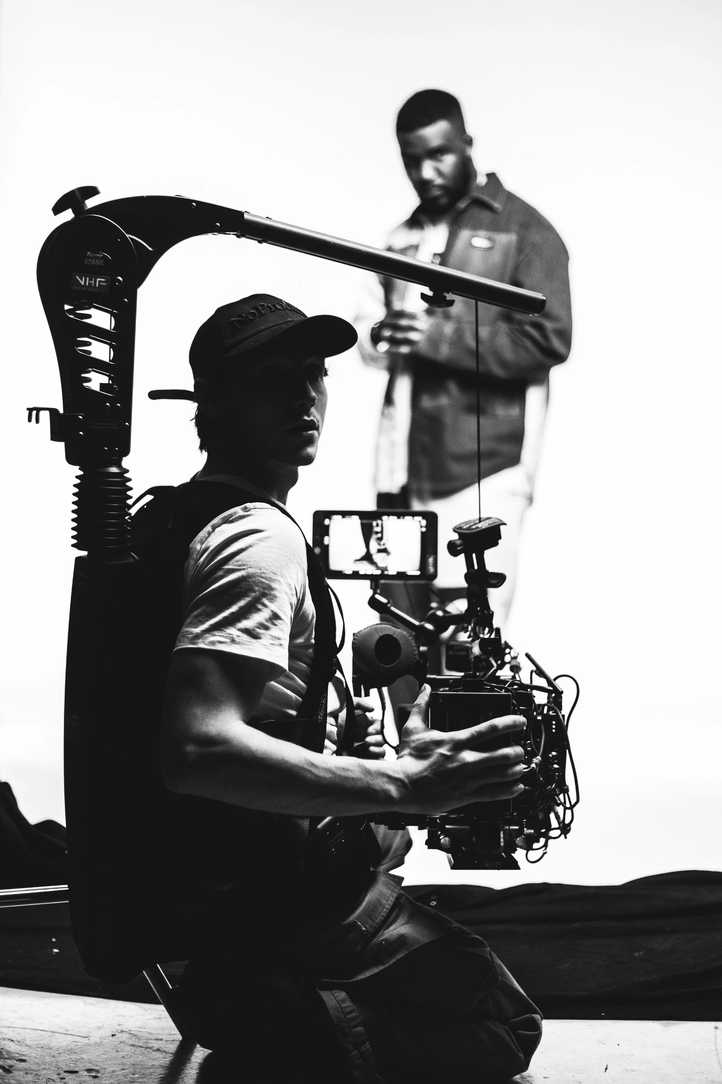 Behind-the-scenes of a film shoot with a camera operator holding a professional camera and a man standing in the background, capturing footage.