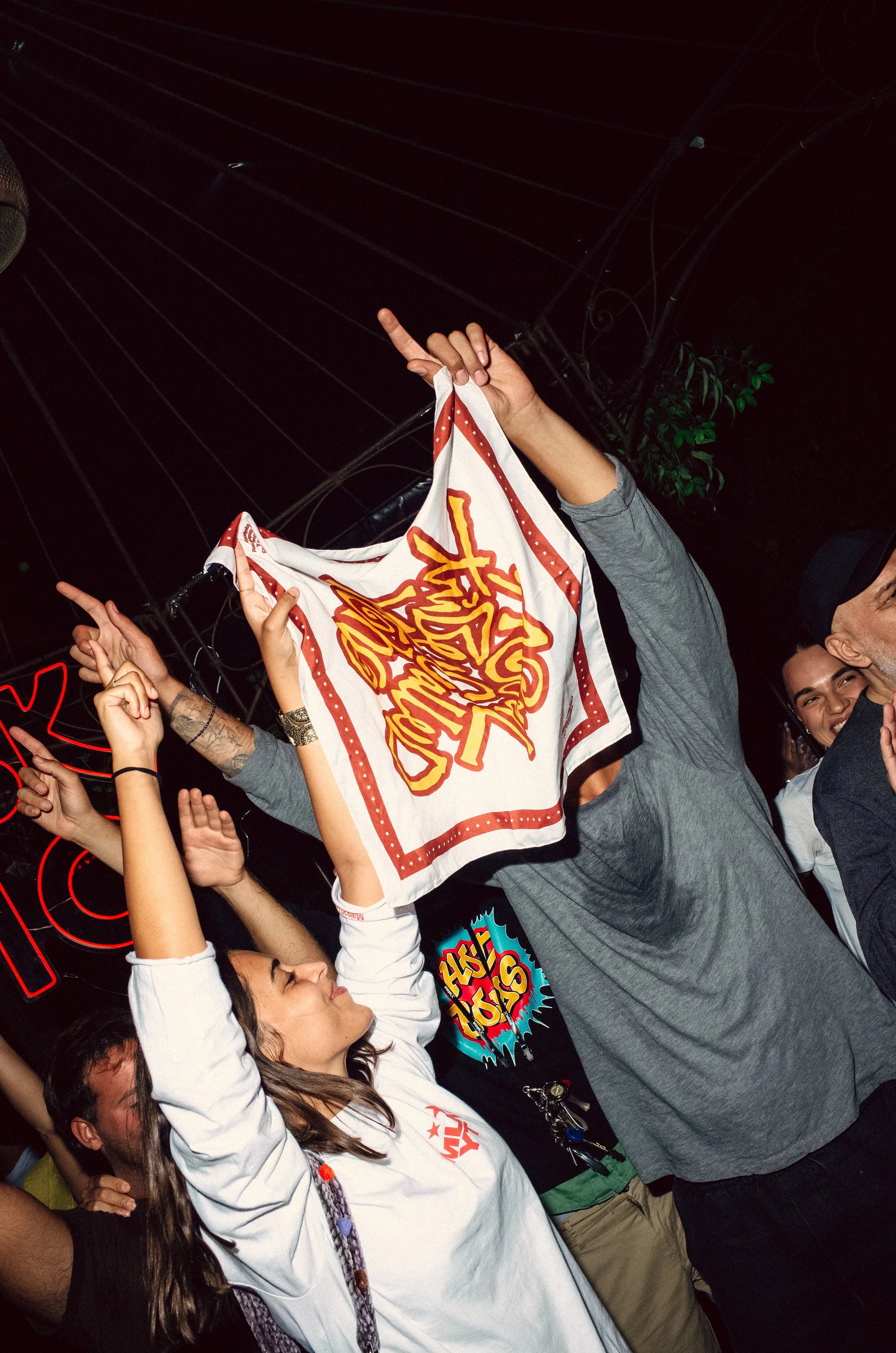 Young woman dancing at a crowded concert, holding a bandana with a colorful design above her head.