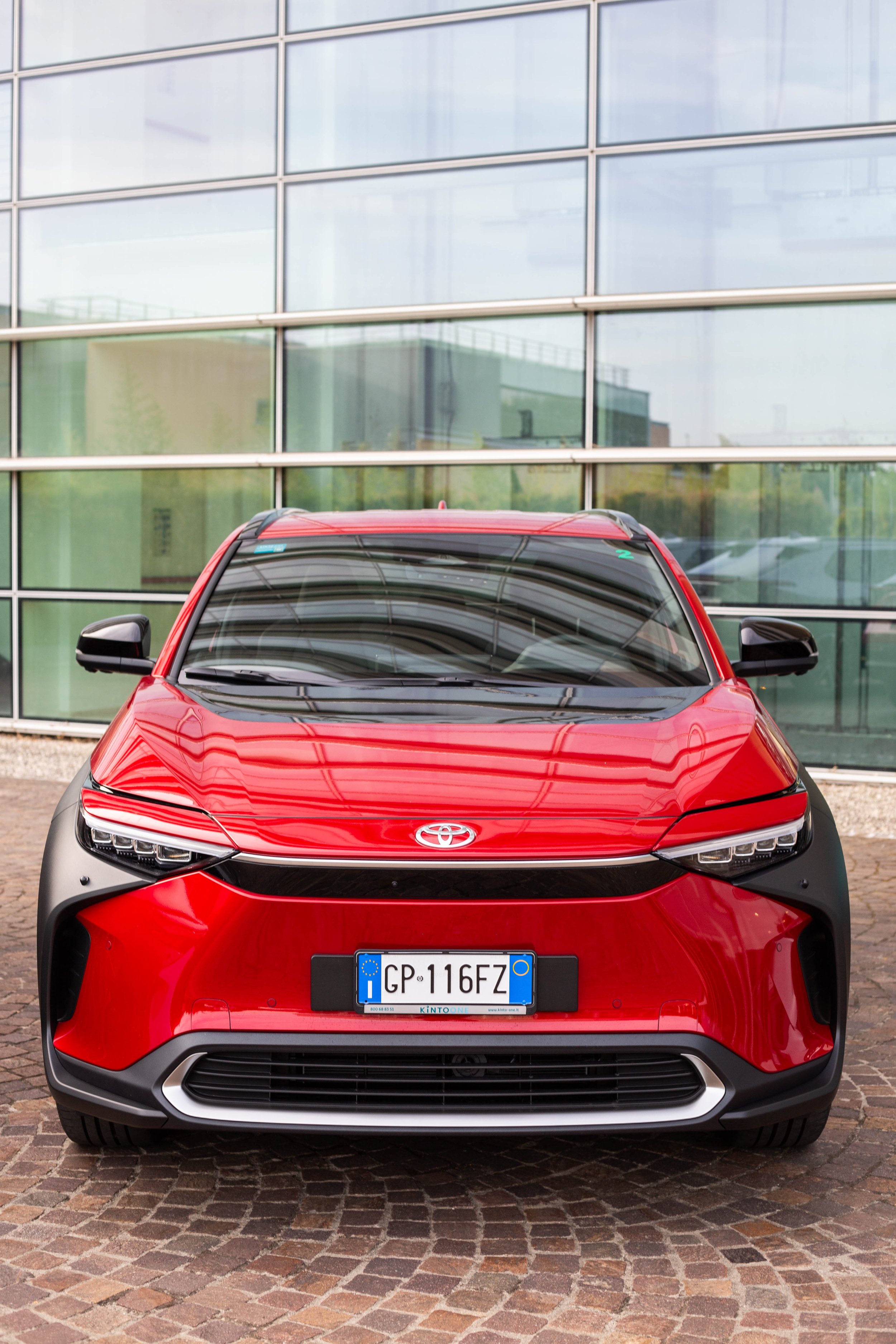 Front view of a red Toyota electric car parked in front of a modern glass building.