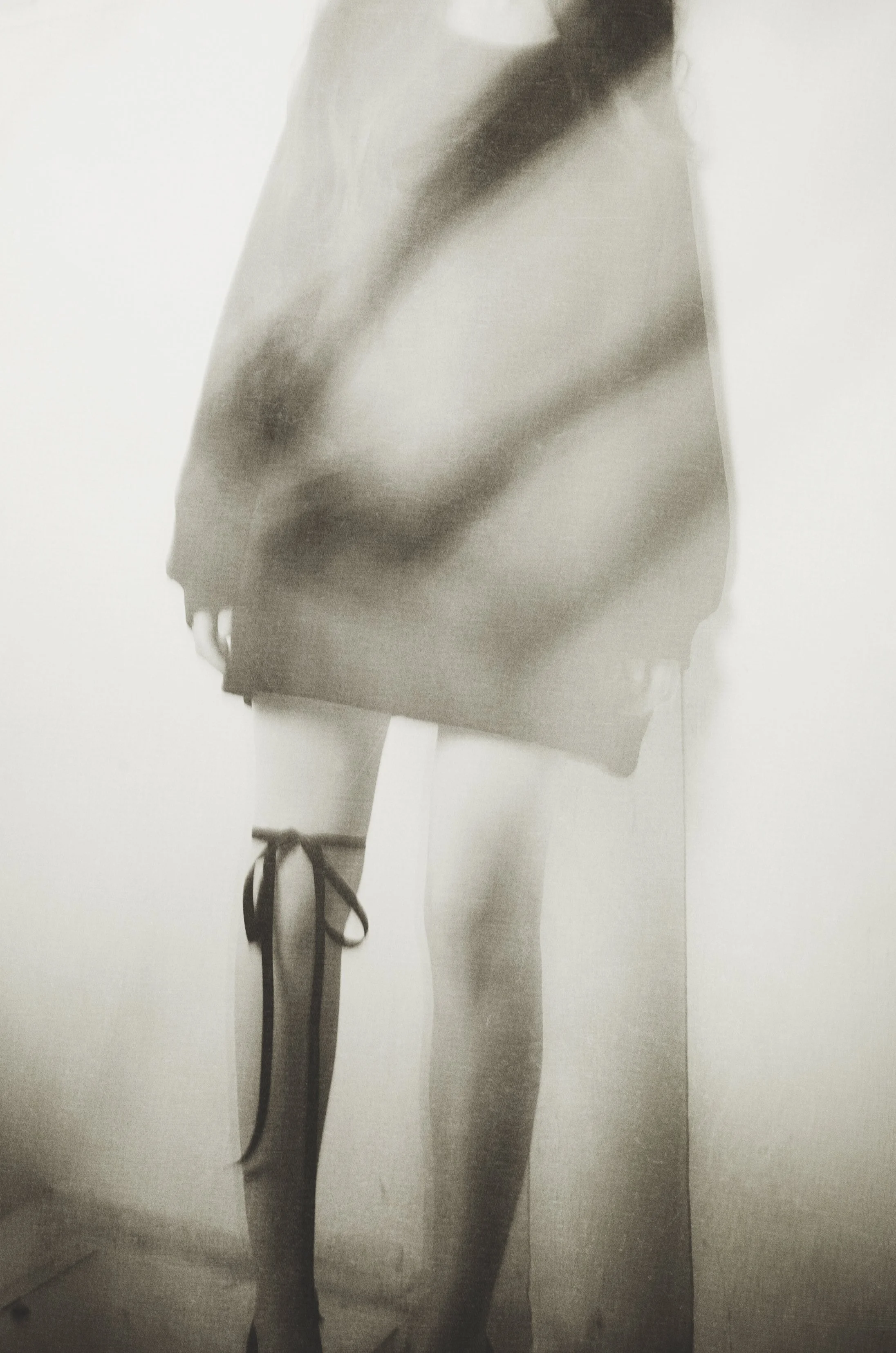 A person wearing a coat, skirt, thigh-high stockings, and high-heeled shoes with tied ribbons on one leg.