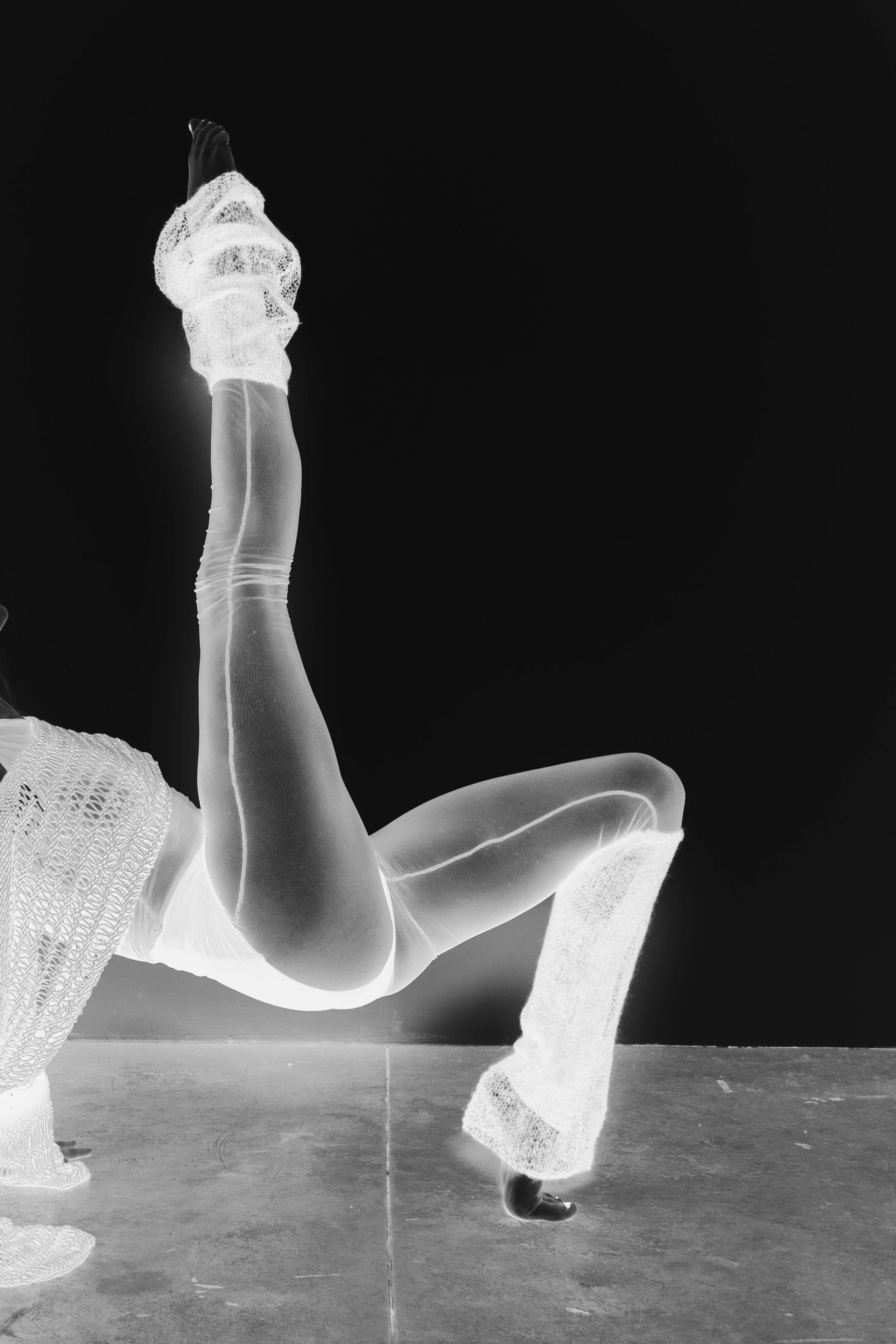 A person is doing a handstand with one arm, wearing textured clothing, and the image is in infrared or negative style making it appear in black and white.
