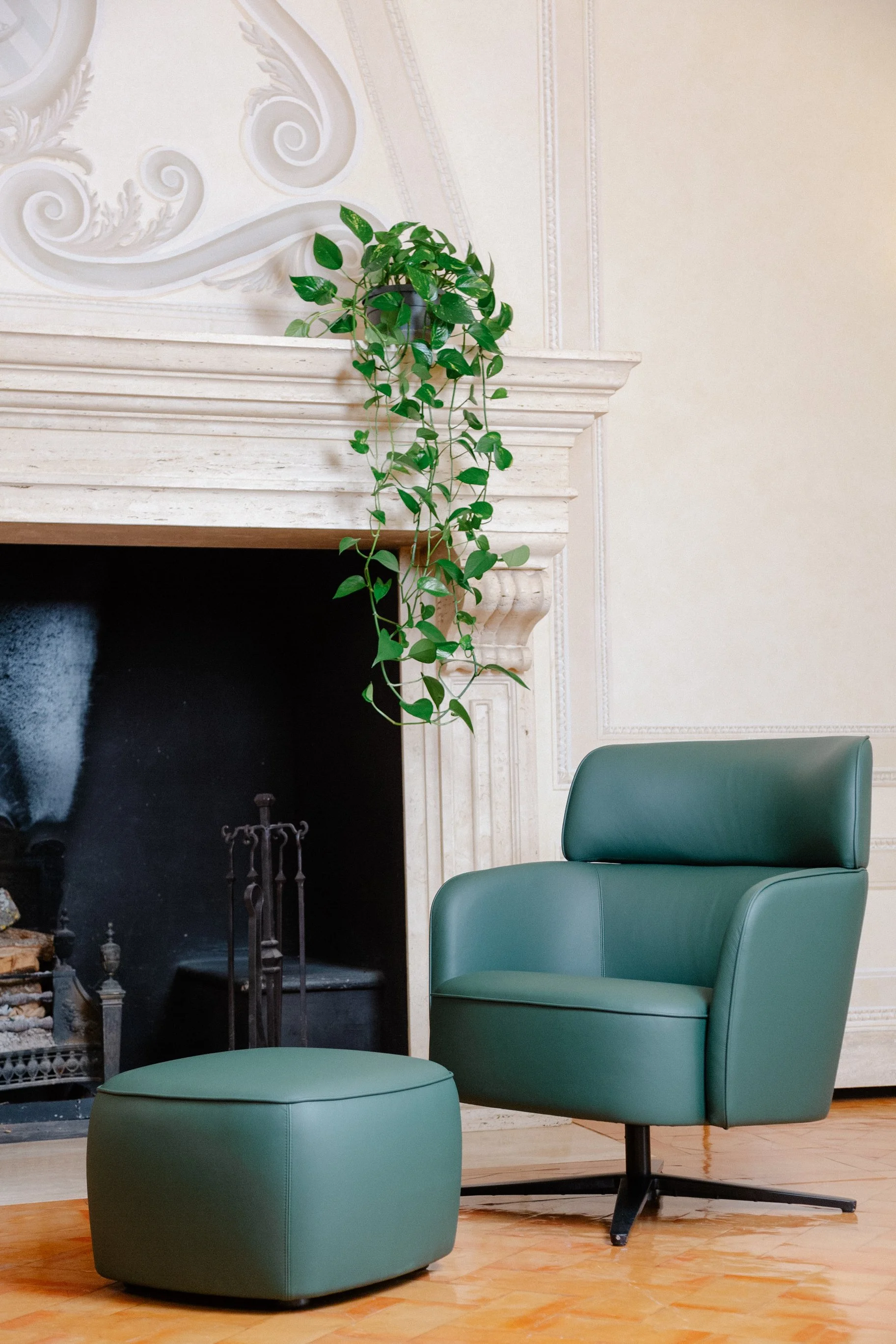 A modern green armchair with matching ottoman next to a fireplace with a green hanging plant above.