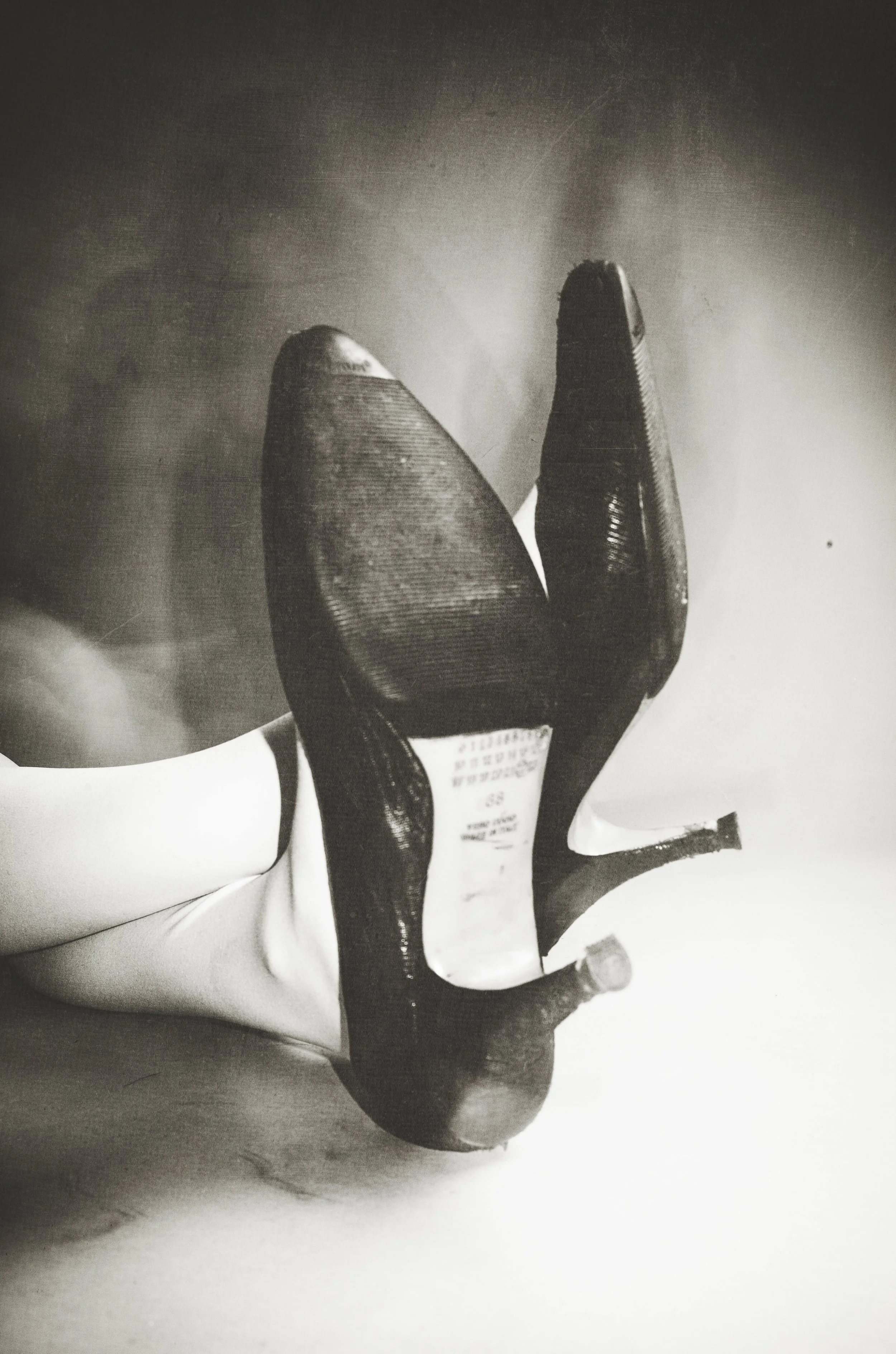 Close-up of a person's leg wearing a high-heeled shoe, viewed from below, in black and white.