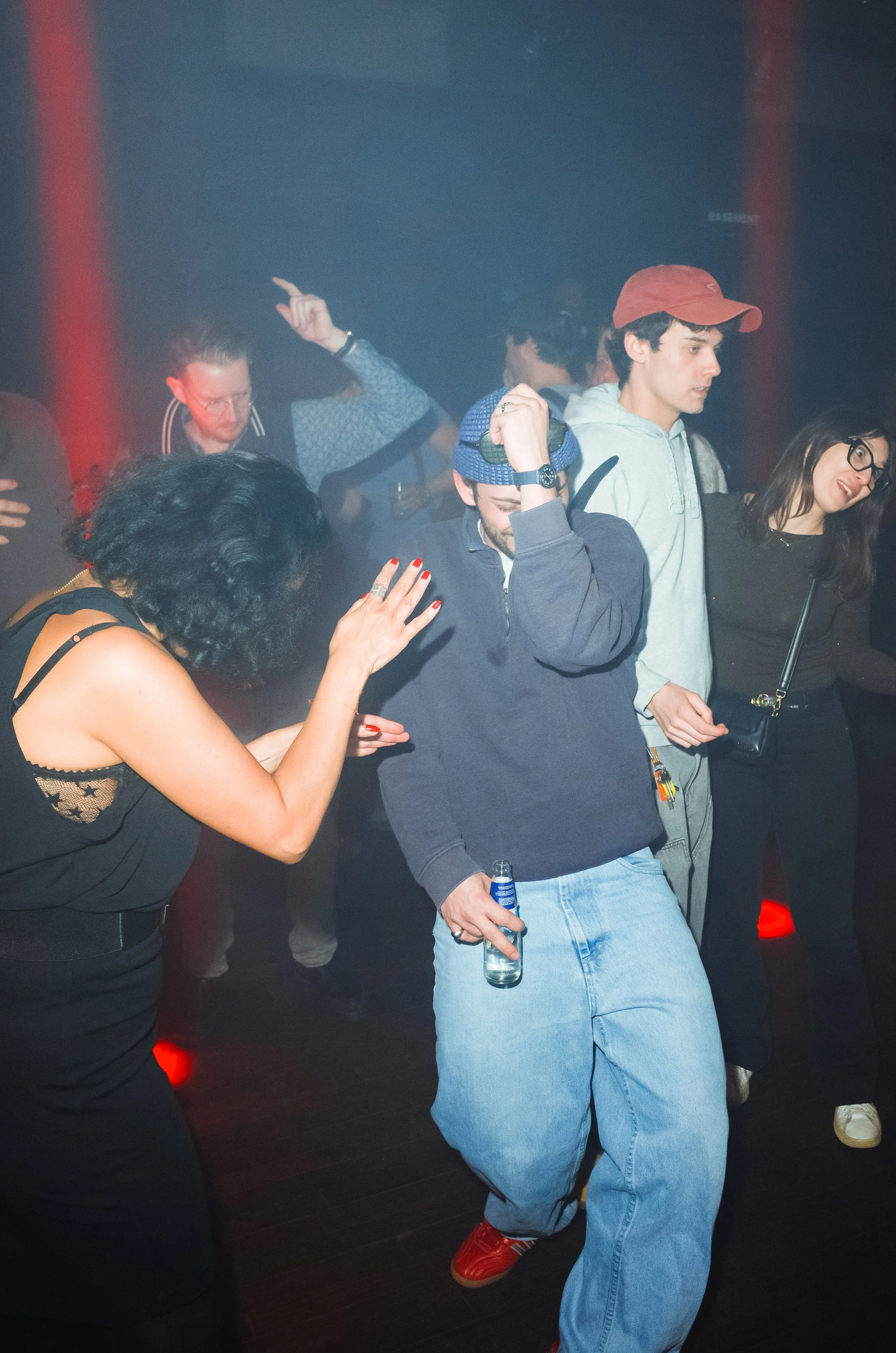 People dancing and enjoying music in a nightclub with red lights and a dark background.