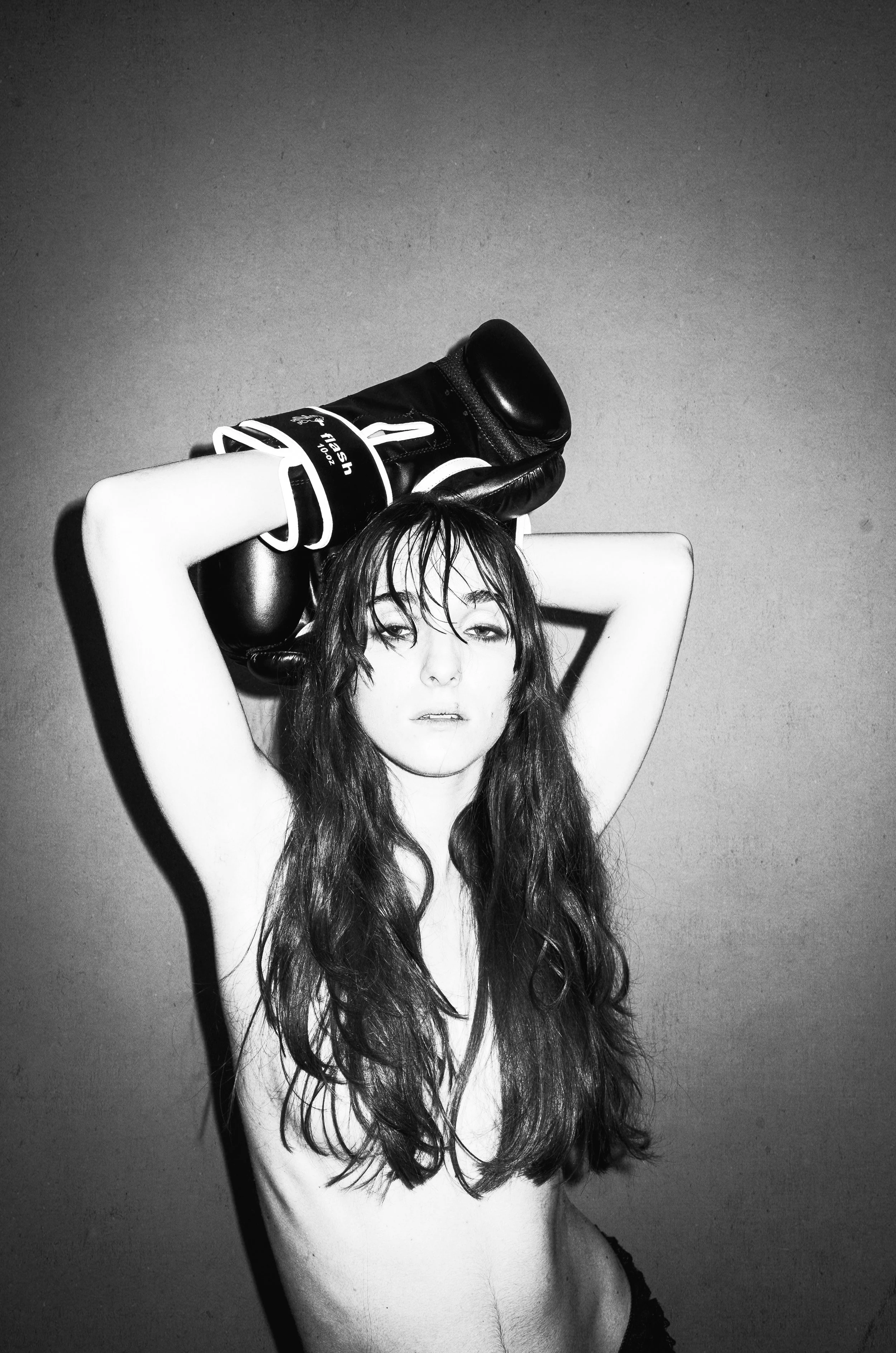 A young woman with long, wavy hair holding boxing gloves above her head, looking confidently at the camera in a black and white photo.