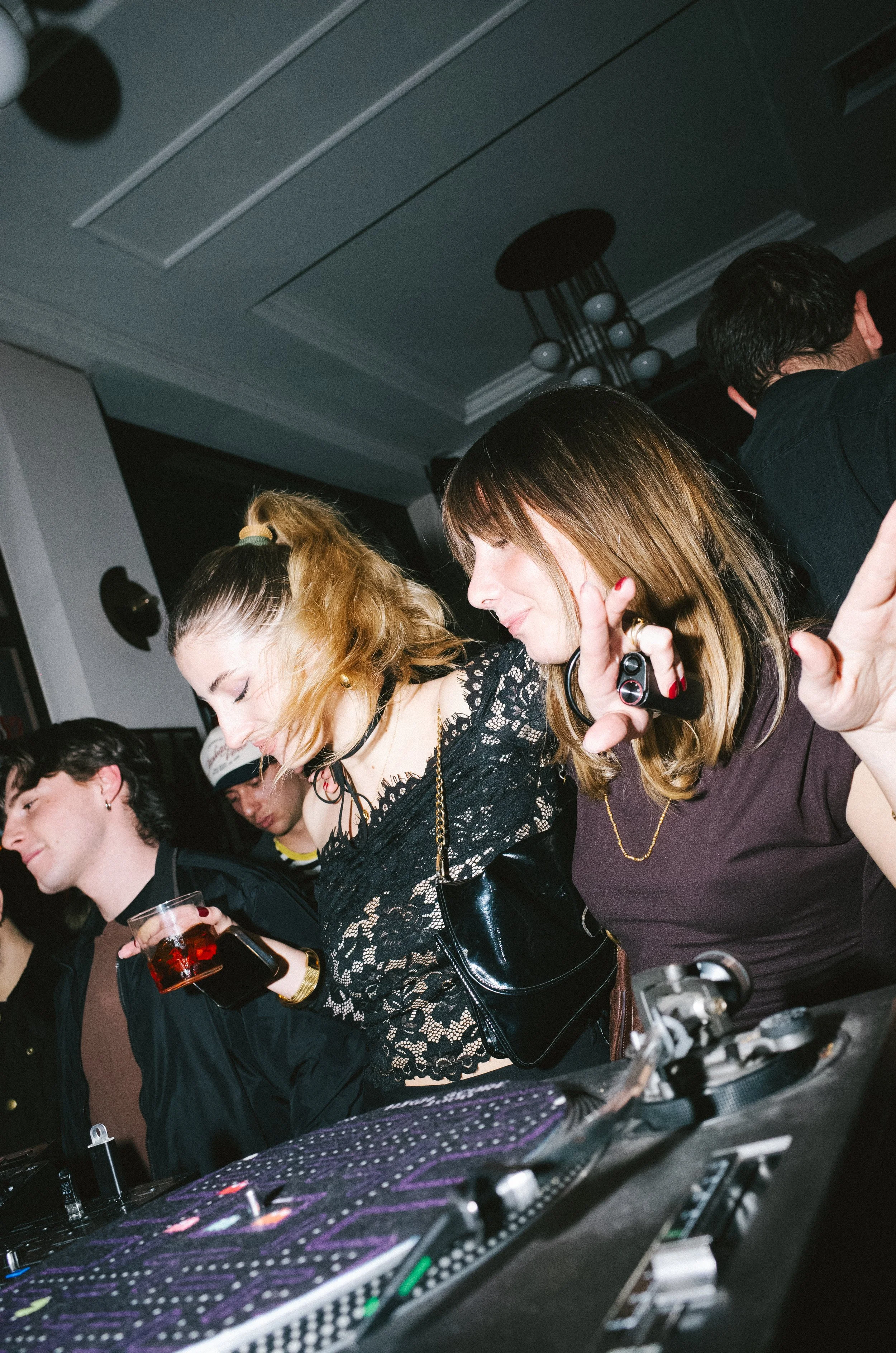 People dancing and enjoying music at a party or nightclub with DJ equipment visible in the foreground.