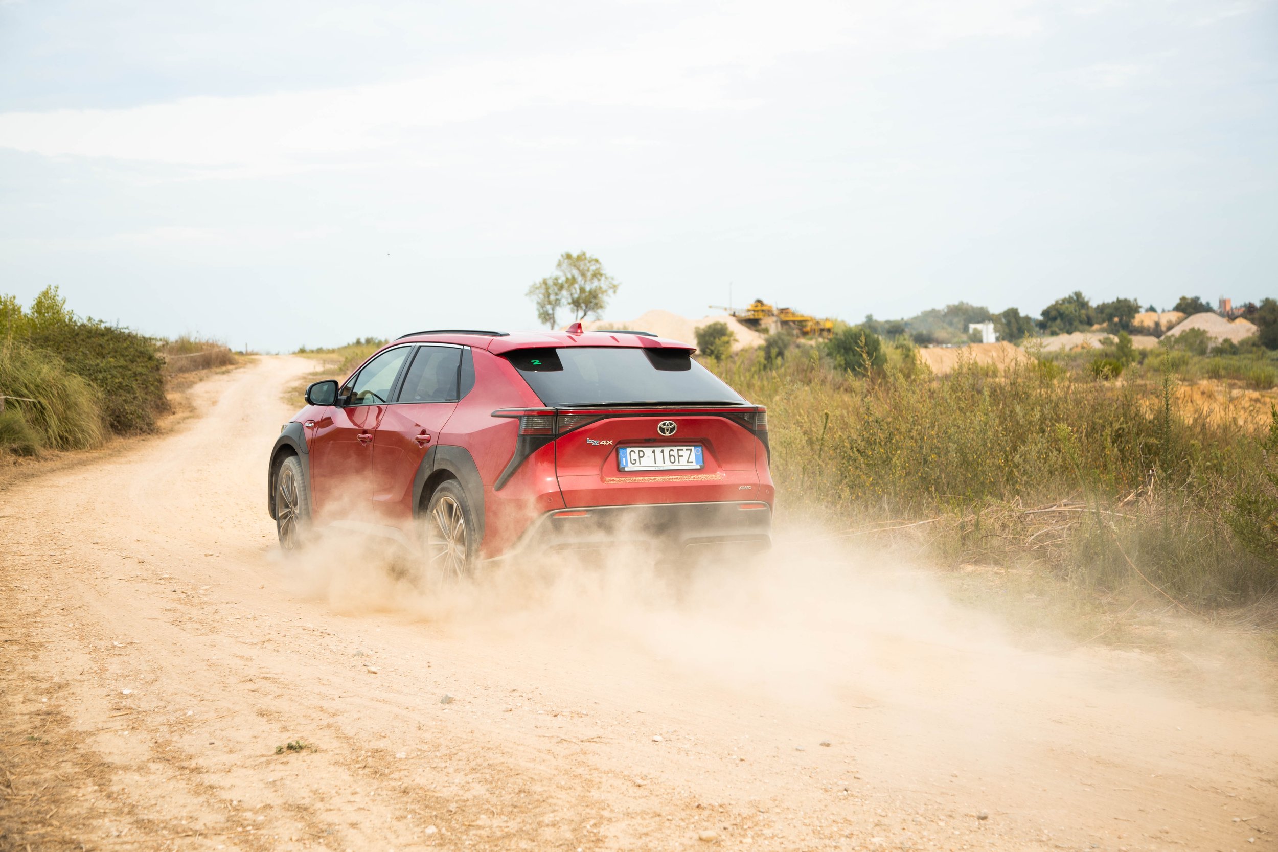 A red Toyota SUV driving on a dusty dirt road in a rural or desert area, kicking up dust behind it.
