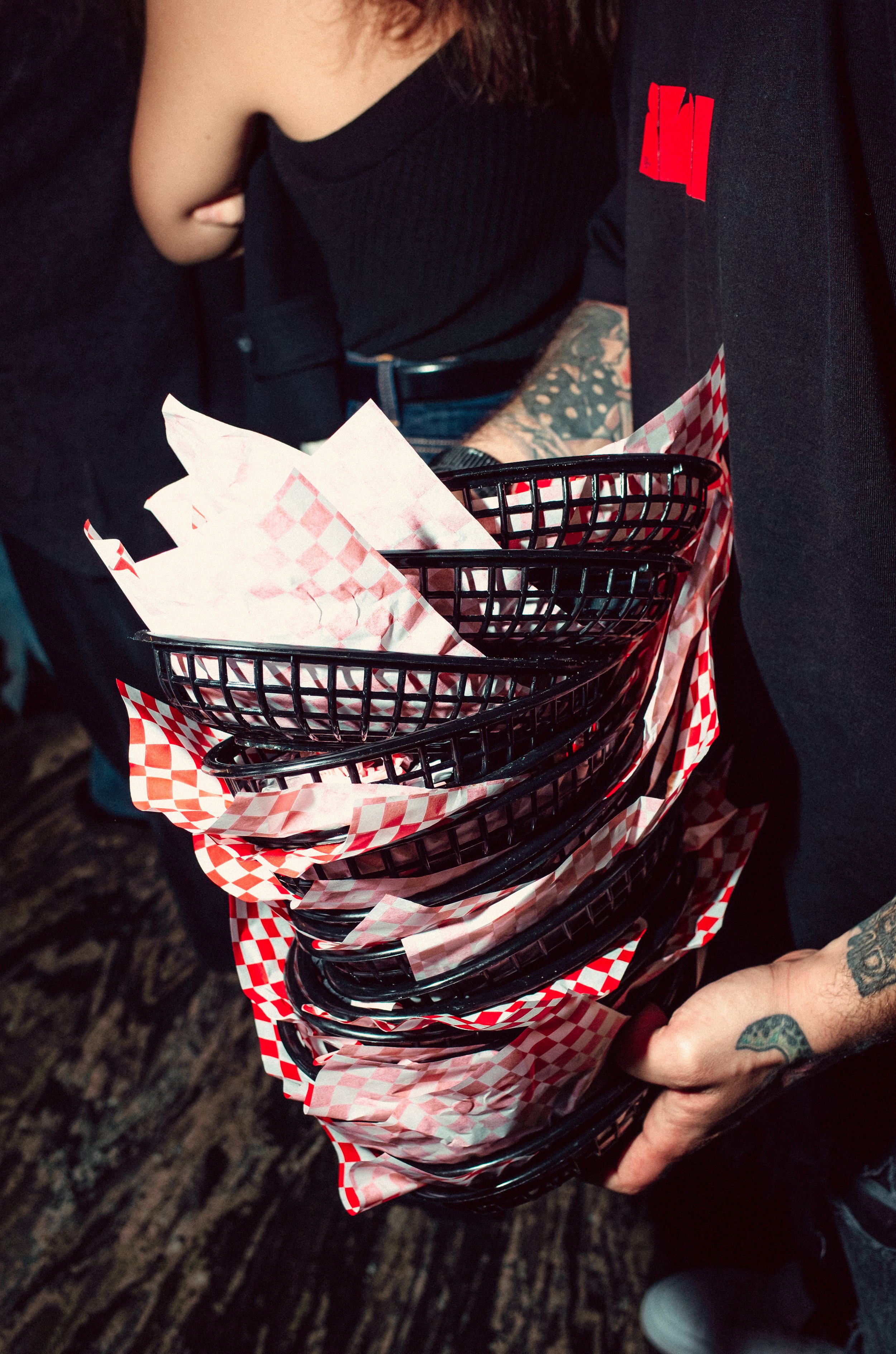 A person holding a stack of black baskets lined with red and white checkered paper, likely used for serving food or takeout at a restaurant.