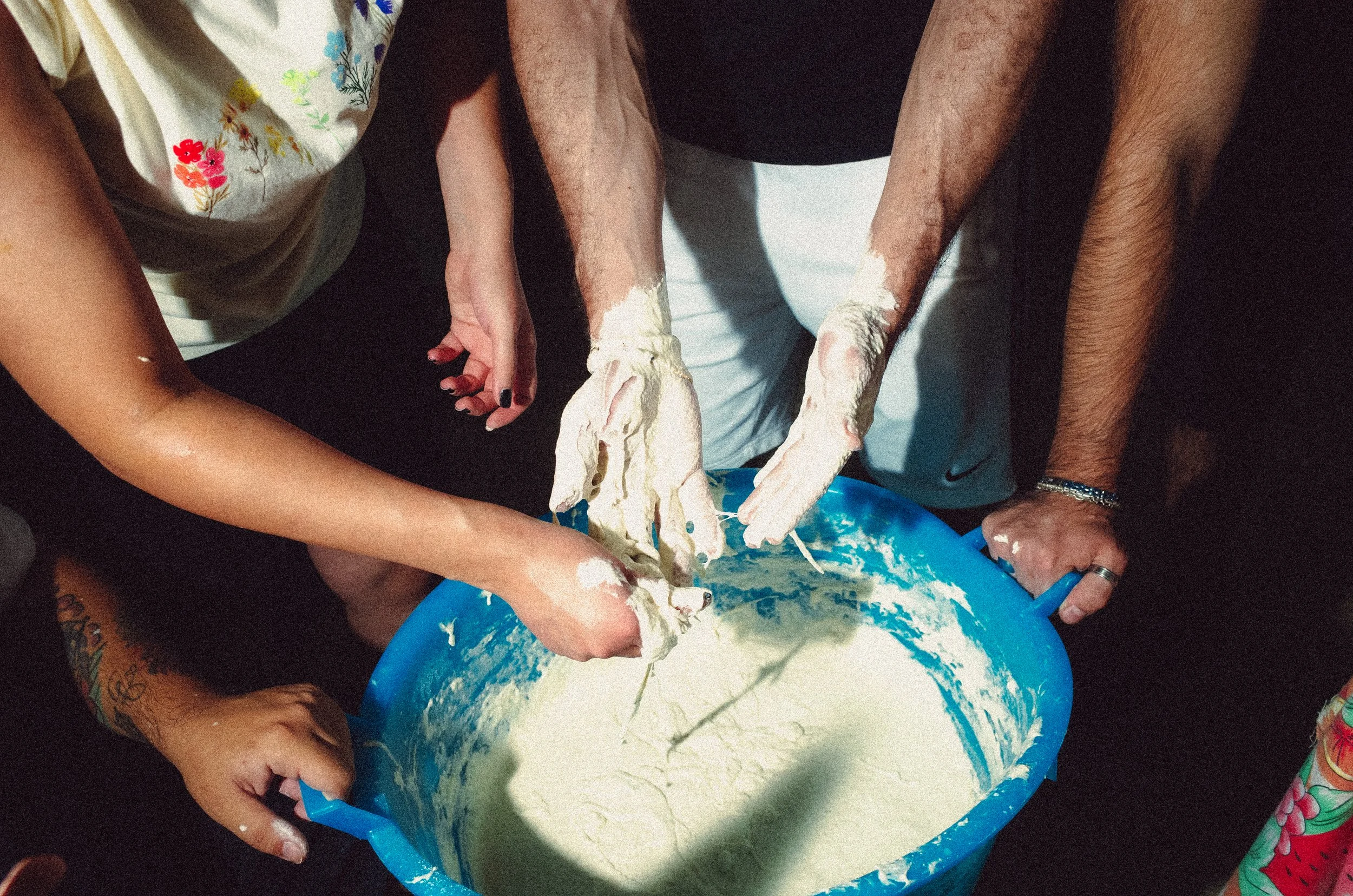 People stirring a large blue bowl of batter with their hands.