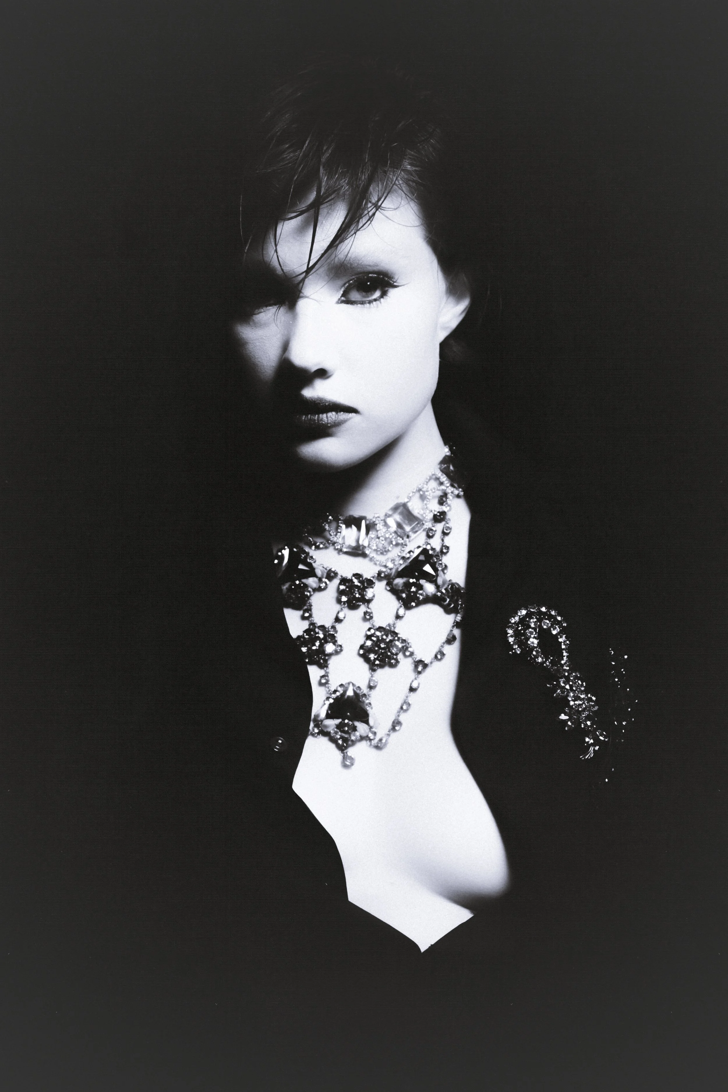 Black and white portrait of a woman with intense gaze, short hair, and wearing elaborate jewelry.