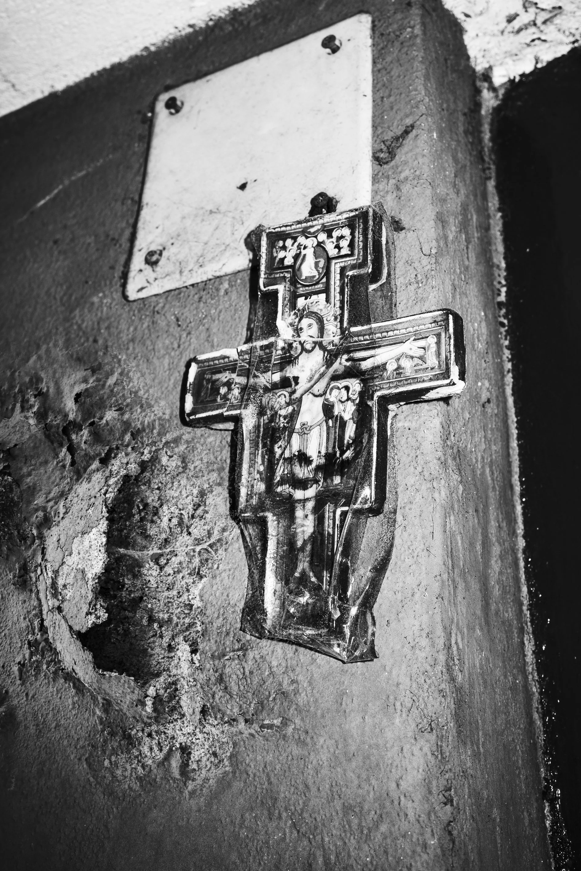 A religious crucifix hanging on a wall next to an empty metal plaque.