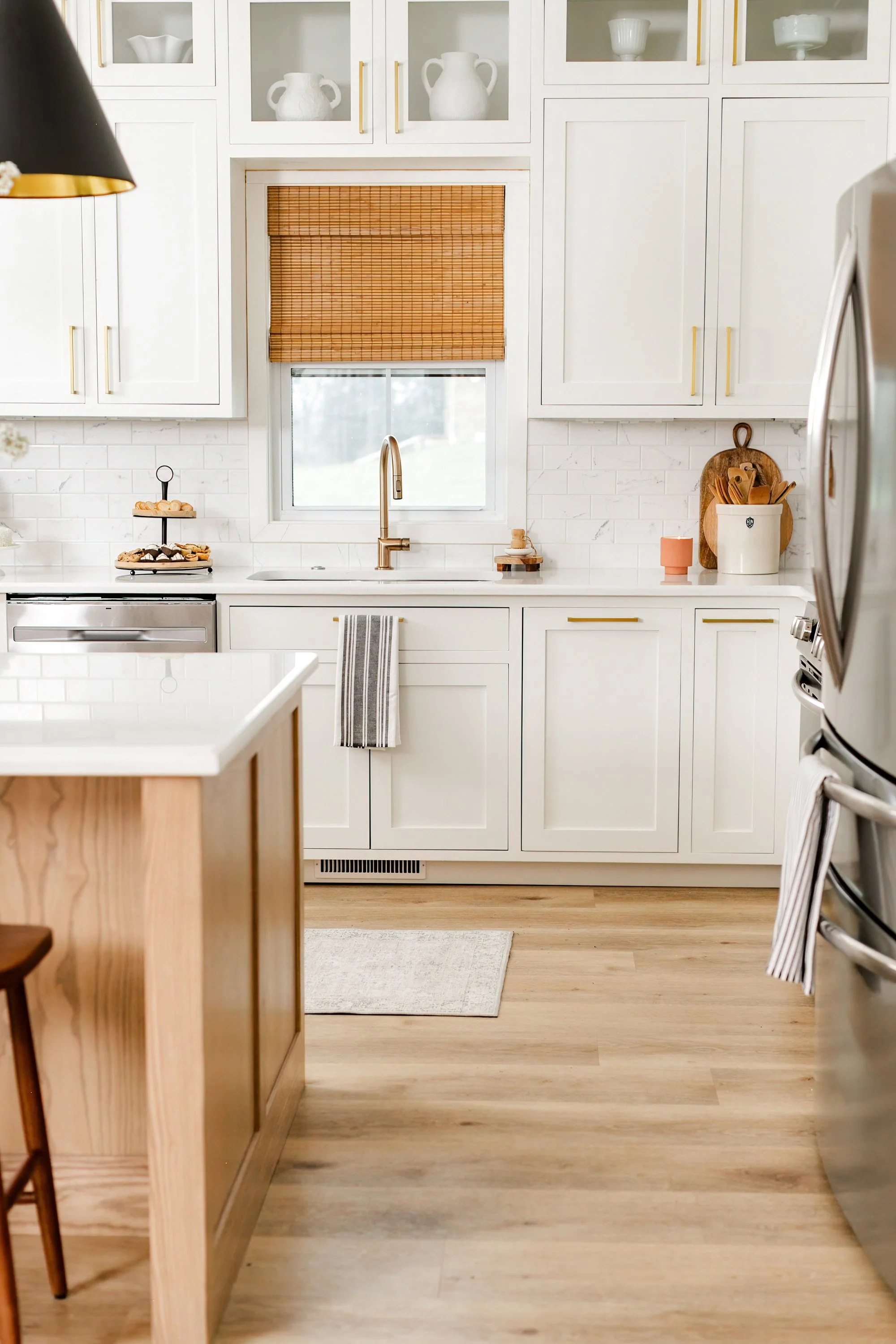 White kitchen with upper cabinets, a window with a bamboo shade, and a wooden island.