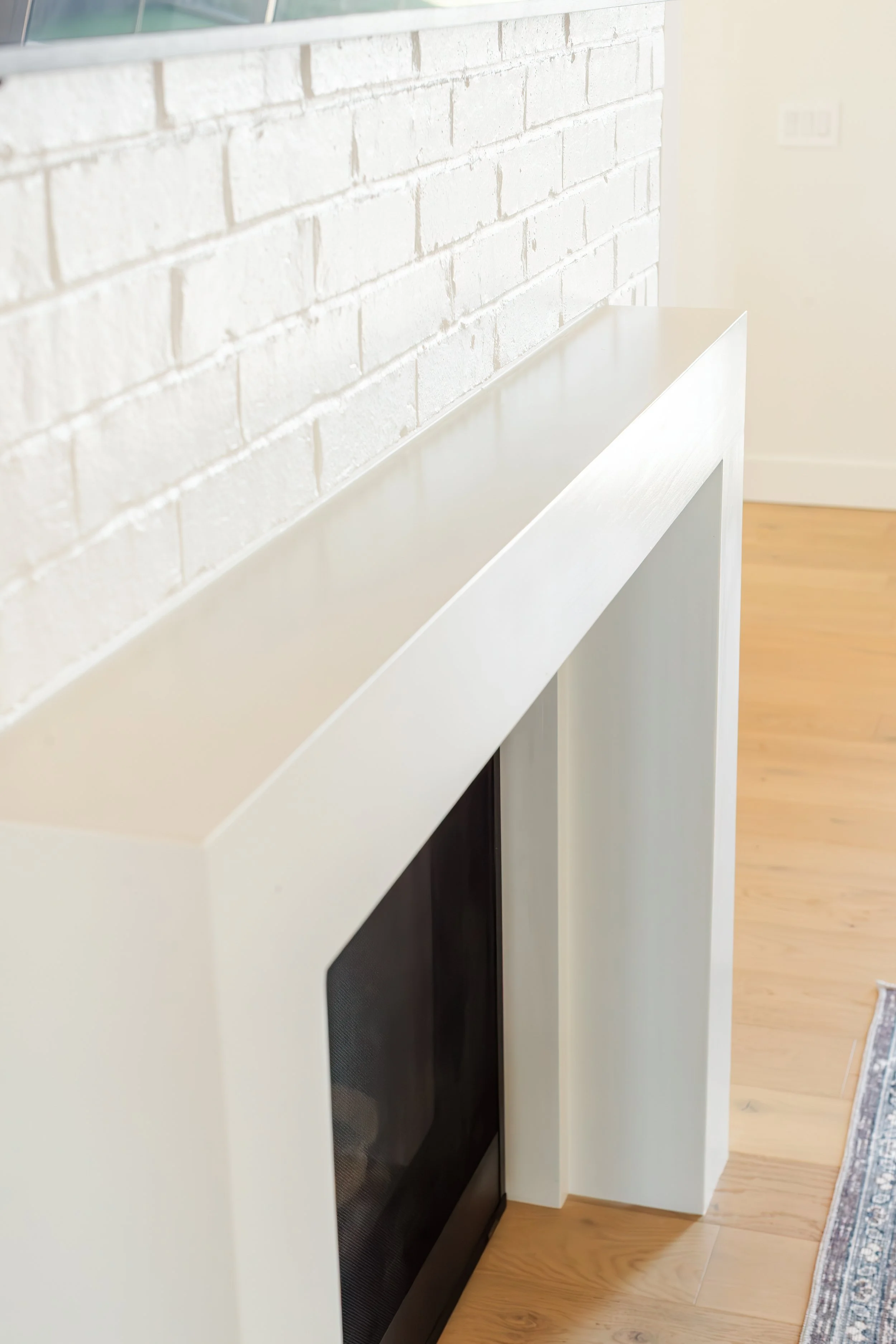 Close-up of a modern fireplace with a white mantle and black interior, set against a white brick wall in a cozy living room.