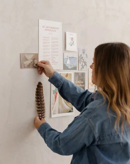 Woman arranging small photos and artwork on a white wall.