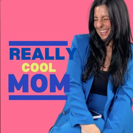 A woman with long dark hair smiling while wearing a blue blazer against a pink background with the words "Really Cool Mom" in blue and yellow text.