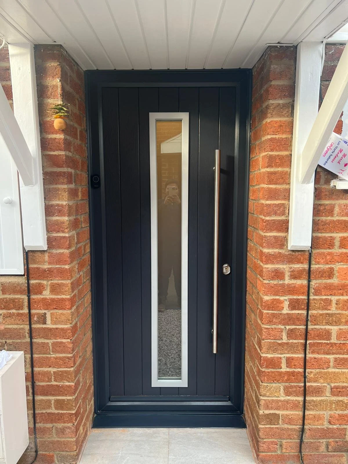 Front door with black paneling, narrow vertical window, metal handle, surrounded by brick walls and white trim.
