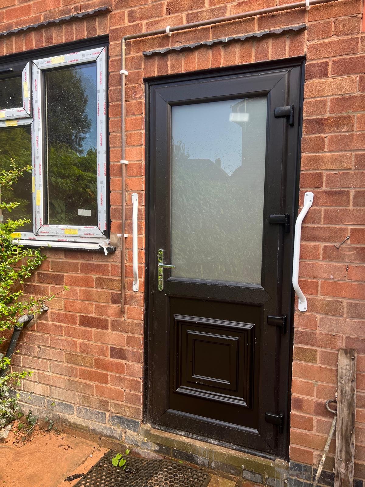 An exterior door with frosted glass on a brick wall, with white grab bars on both sides, and a small mat on the ground outside.