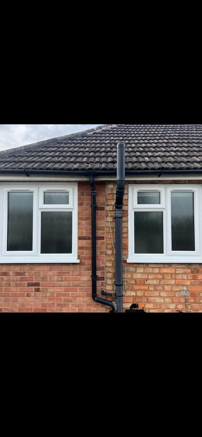 Close-up of a brick house exterior with two white-framed windows and black drainpipes running down the wall.