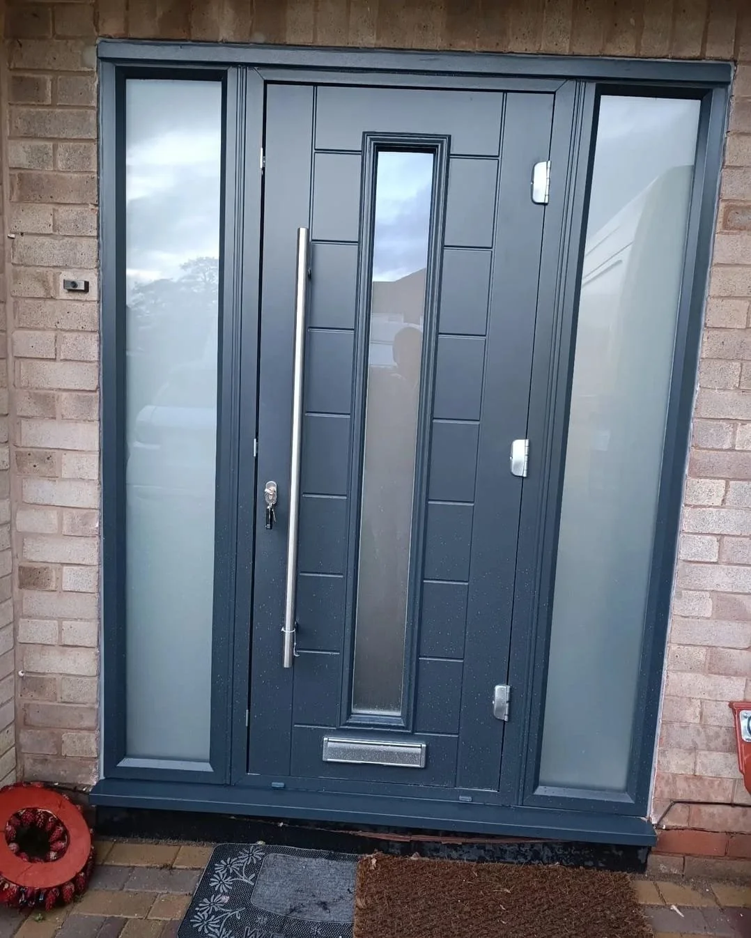 Black front door with a vertical glass panel in the center, flanked by frosted glass side panels, set in a brick wall.
