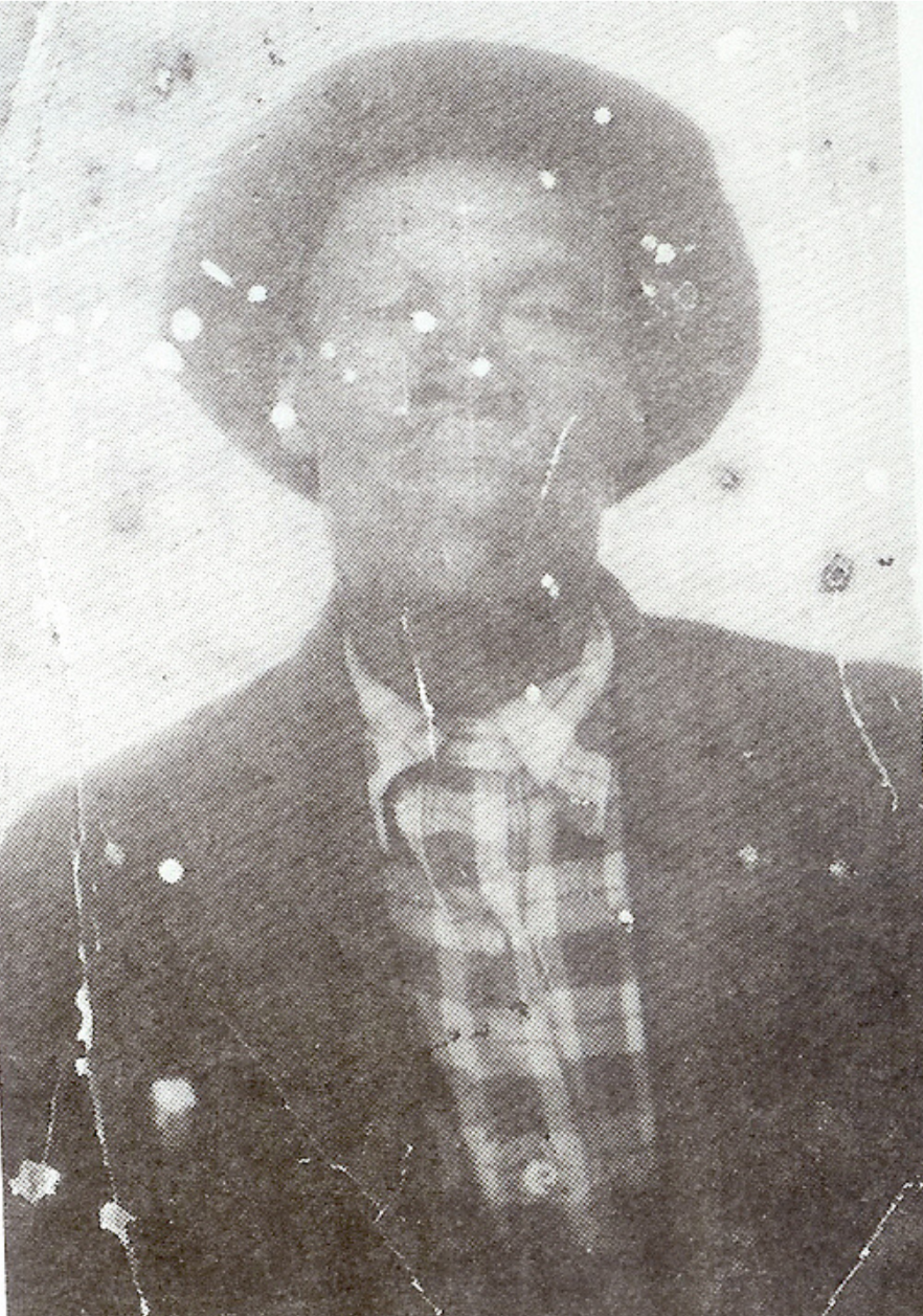 Black and white photograph of a person wearing glasses, a hat, a plaid shirt, and a dark jacket, with weathered and worn appearance.