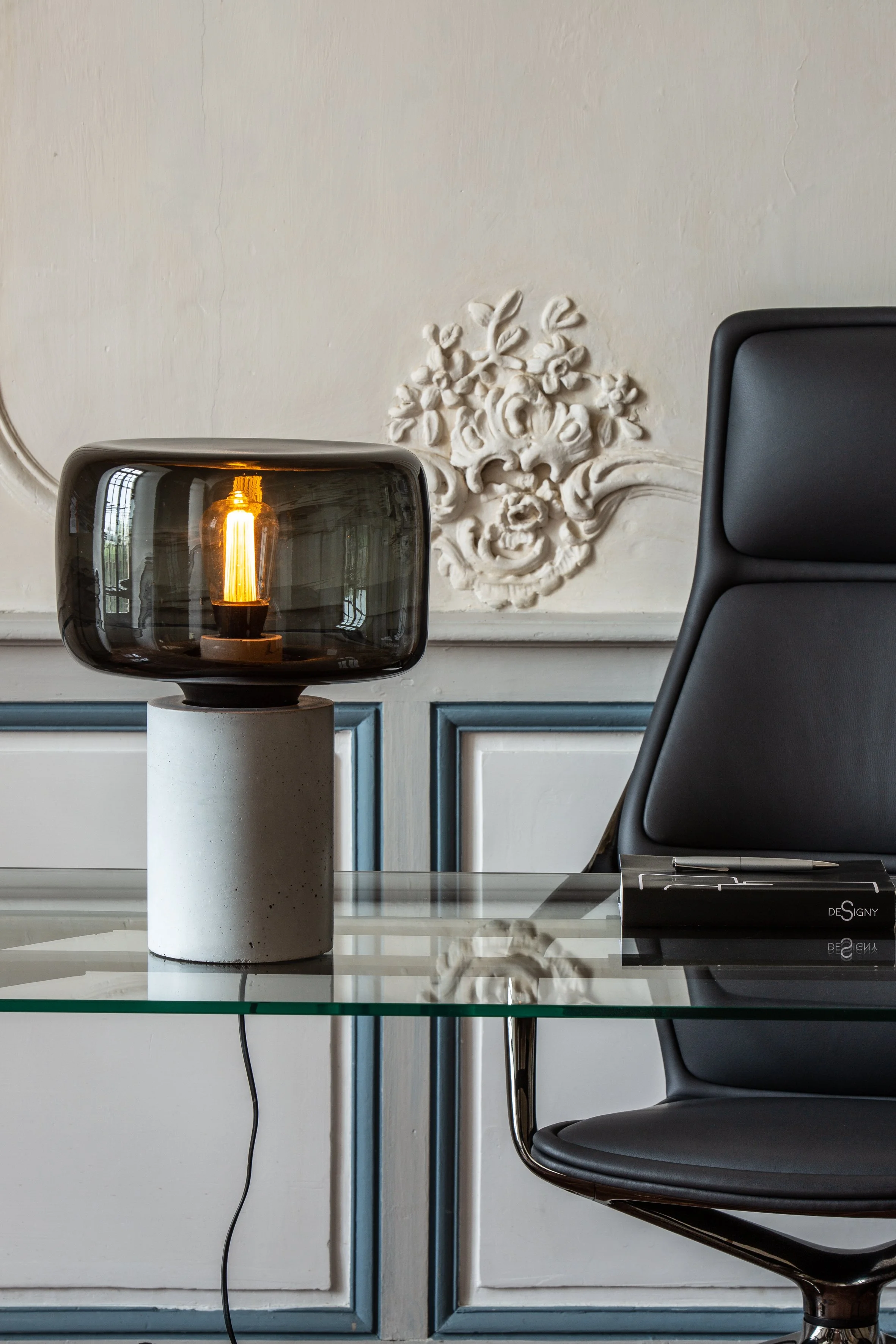 Lampe de table noire avec abat-jour en verre foncé sur un meuble en béton, dans un bureau élégamment décoré.
