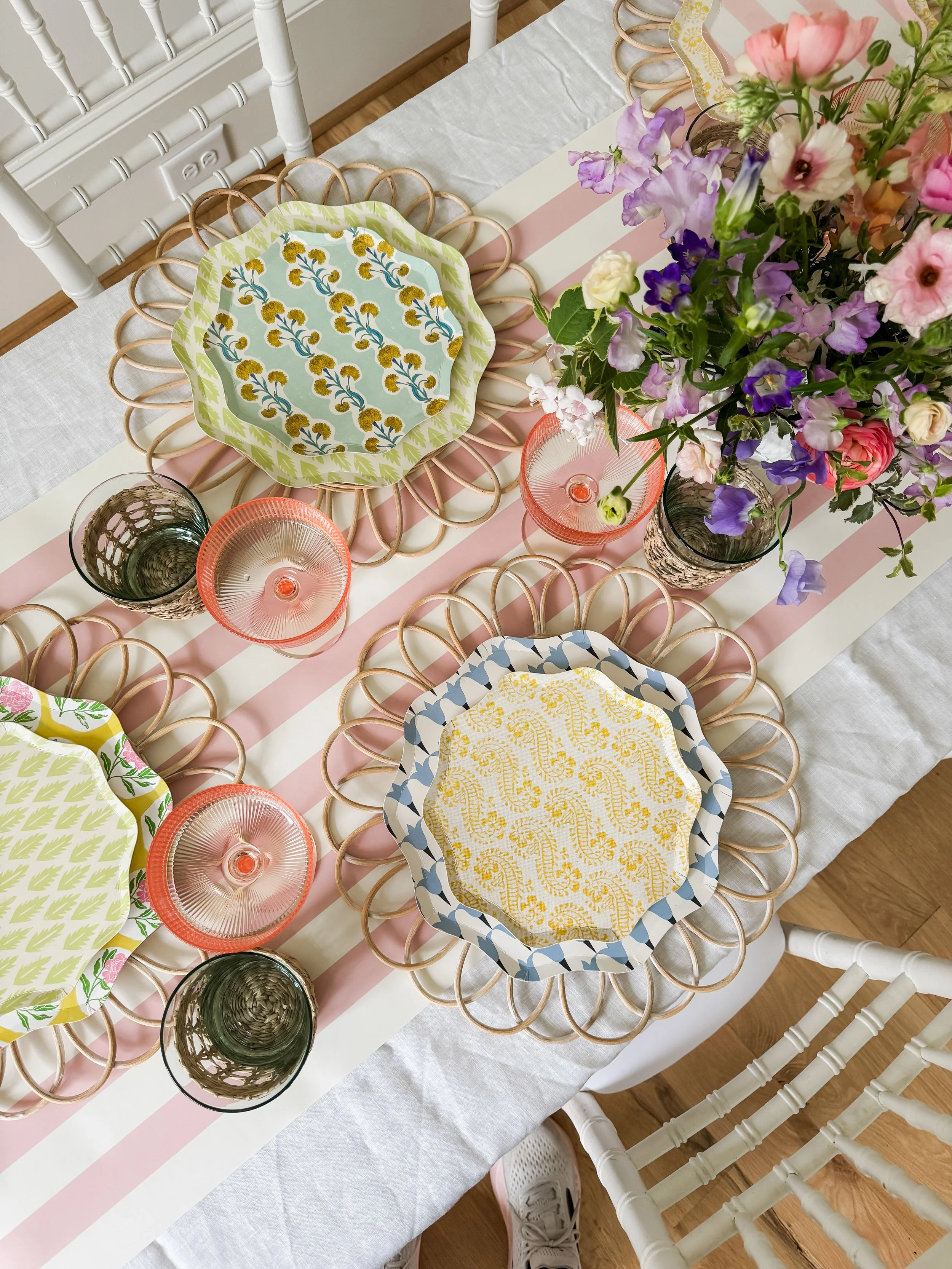 A table set with decorative plates, glasses, and a floral centerpiece with pink, purple, and white flowers.