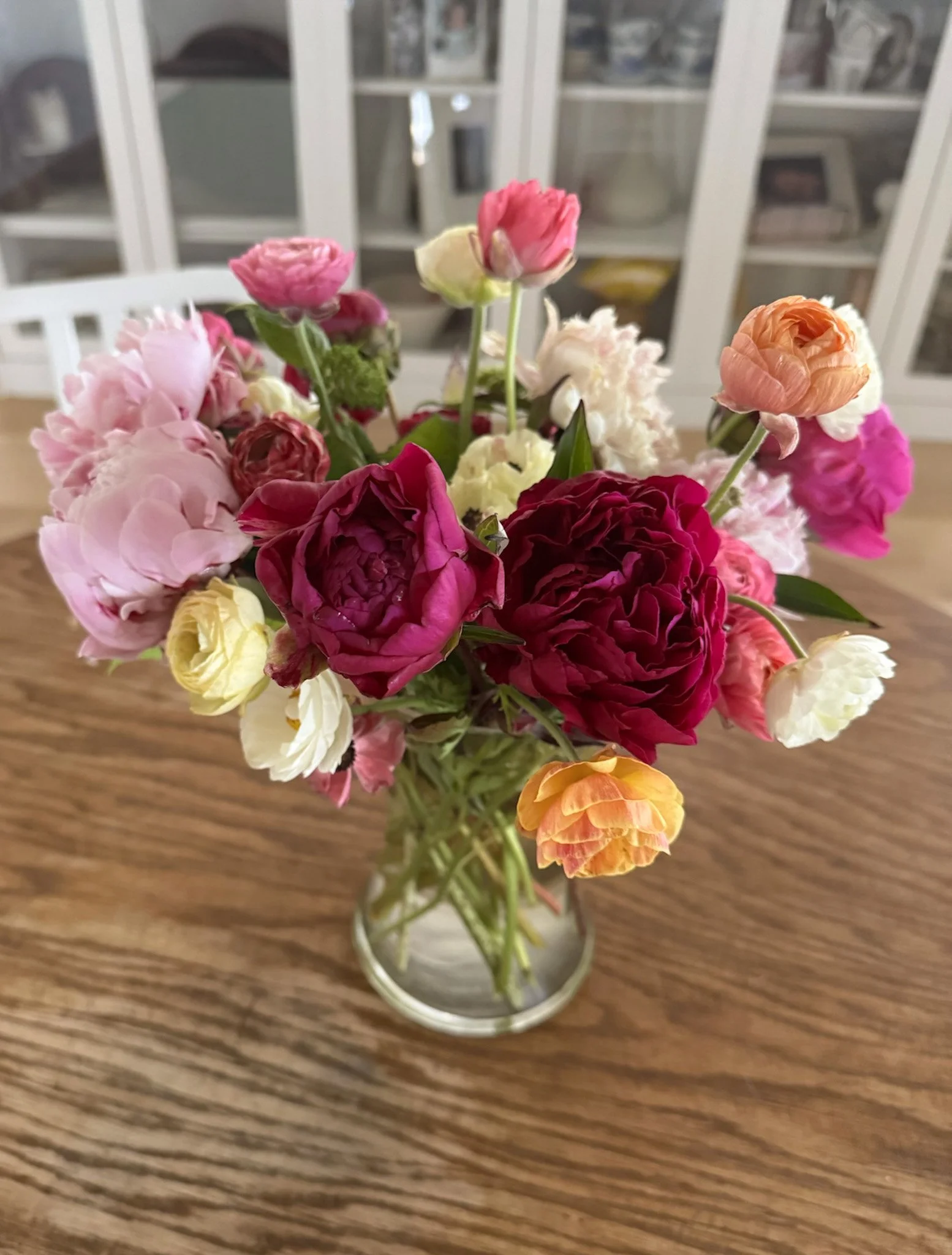 Colorful bouquet of mixed peony flowers in a glass vase on a wooden table.