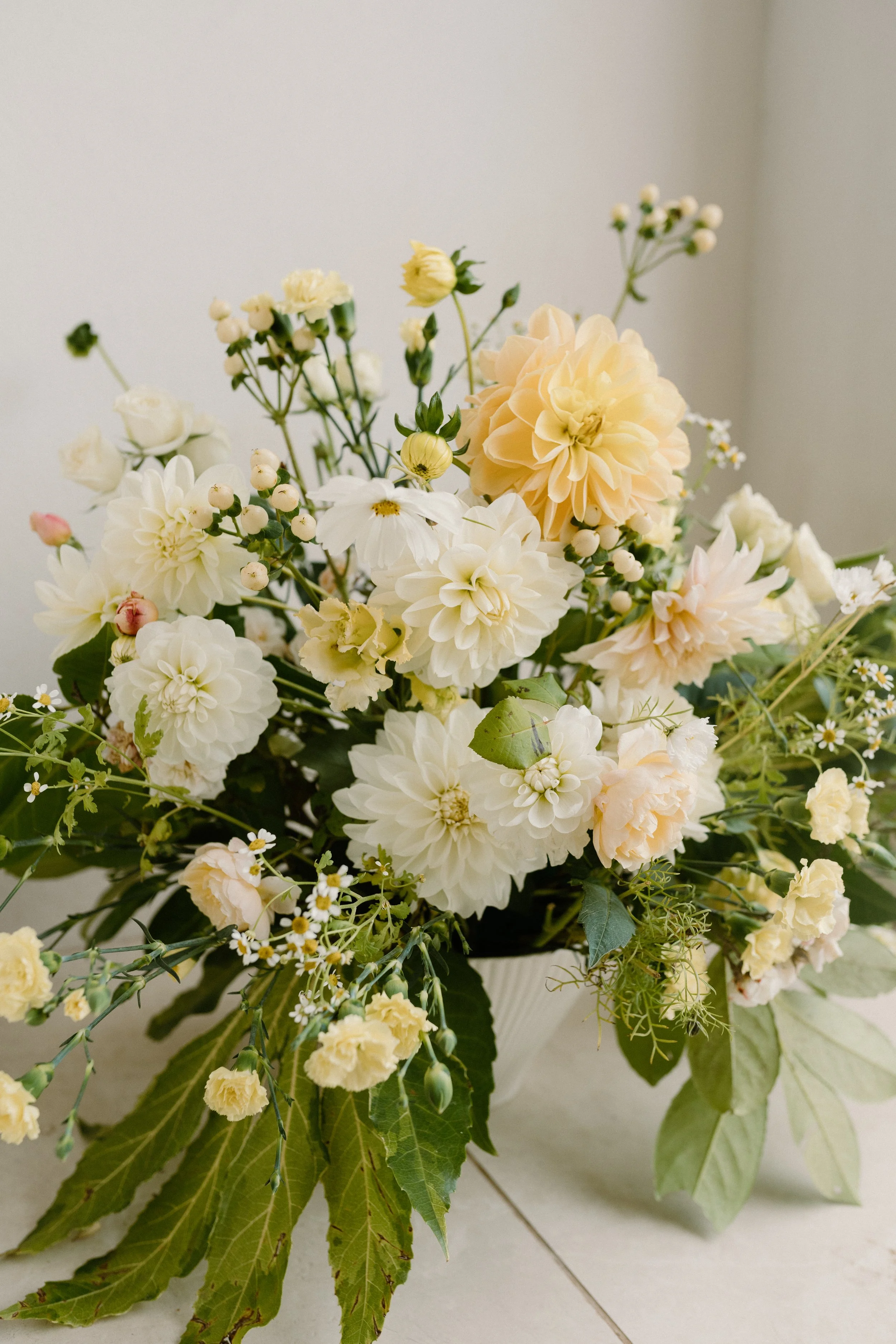 A bouquet of pale yellow and white flowers in a glass vase on a white surface.