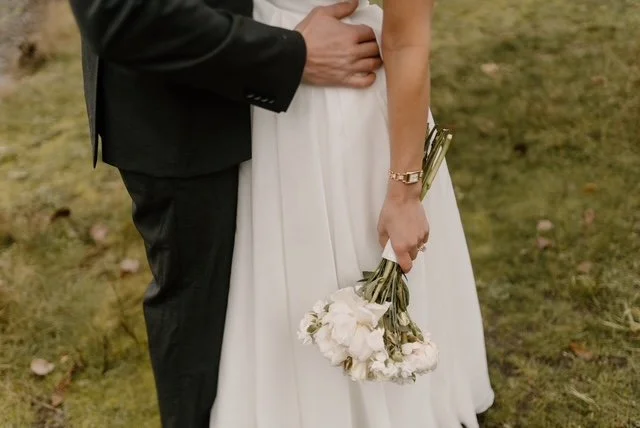 Part of a bride and groom at a wedding, with the bride holding a bouquet of white flowers.