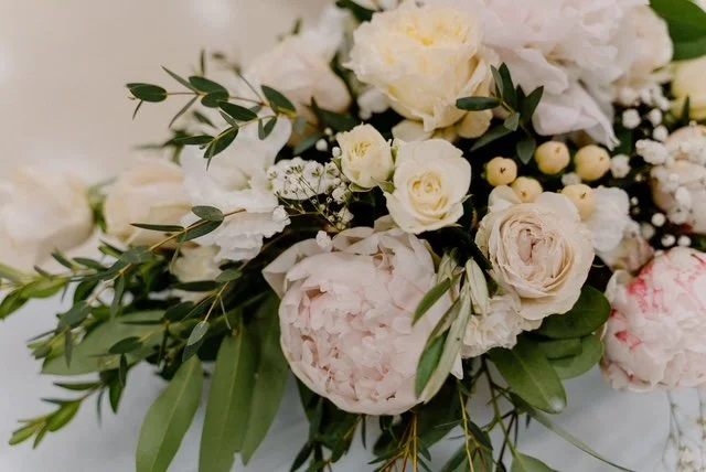 A bouquet of white and pale pink flowers with green leaves and small white berries.