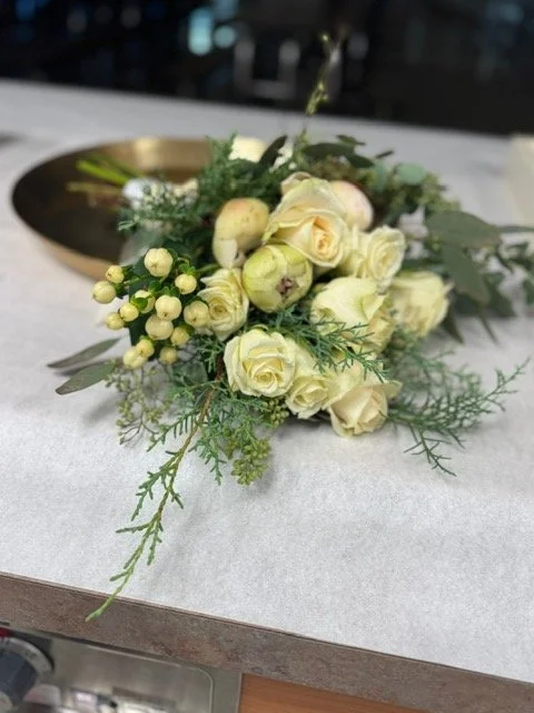 A bouquet of white and cream roses with greenery on a white surface.