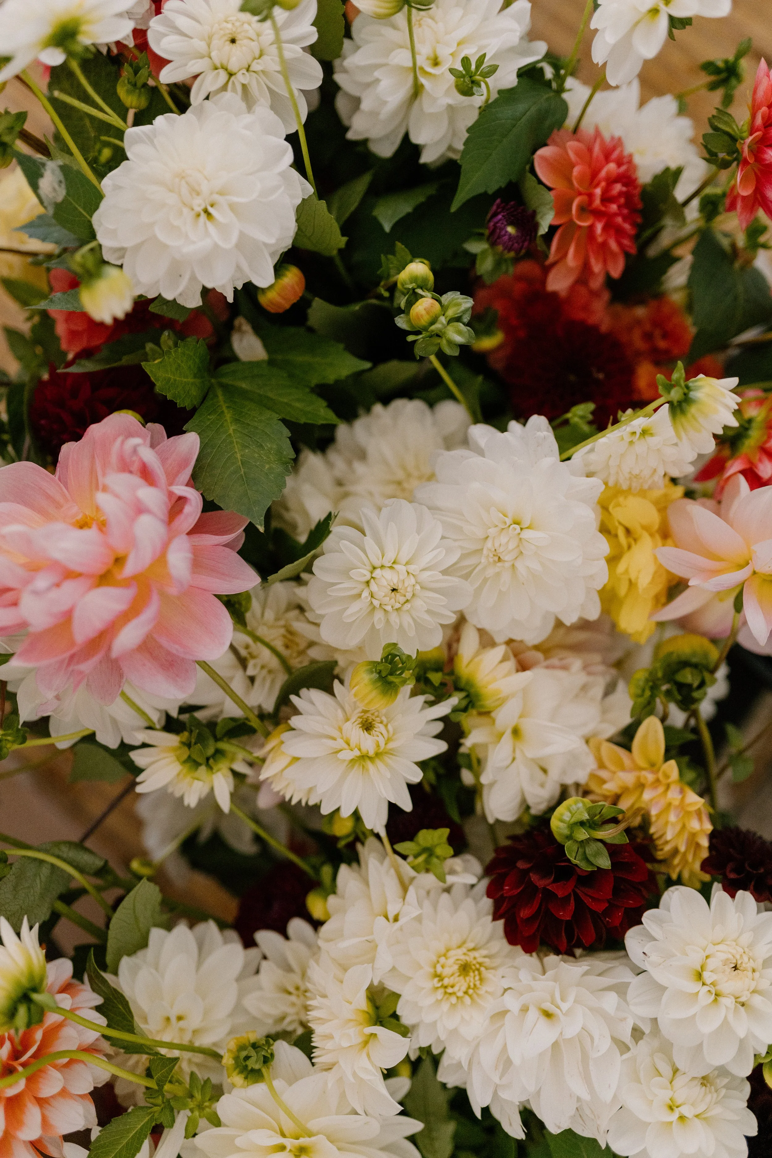 A colorful bouquet of various flowers, including white, pink, red, yellow, and peach blossoms with green leaves.