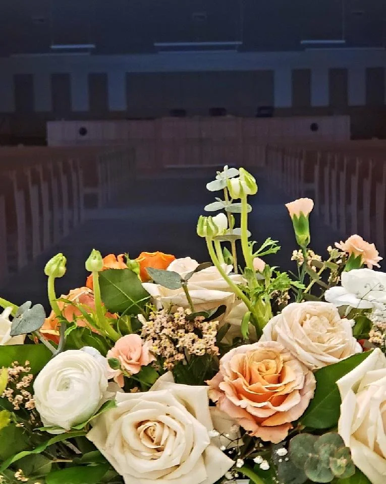 A bouquet of white, peach, and orange roses with greenery, against a dark background.