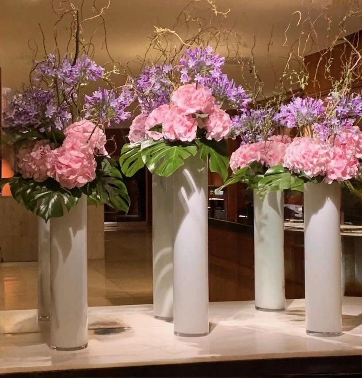 Four white vases with pink and purple floral arrangements on a wooden surface.