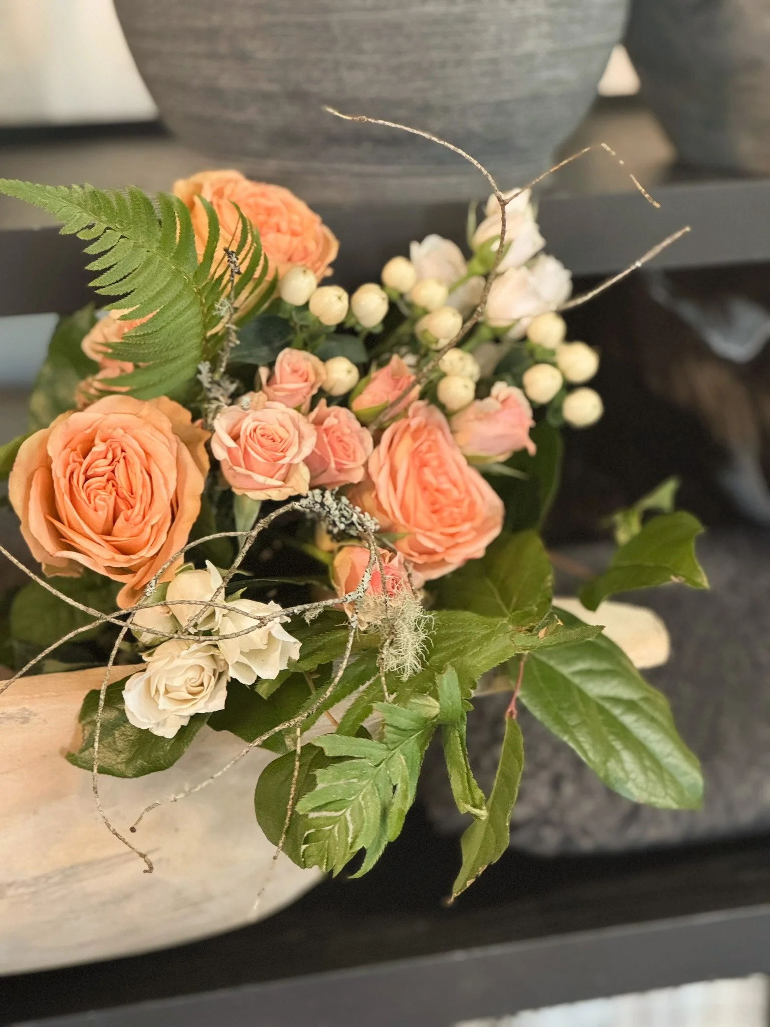 A floral arrangement with pink roses, white berries, eucalyptus leaves, fern, and decorative silver twigs in a white container.
