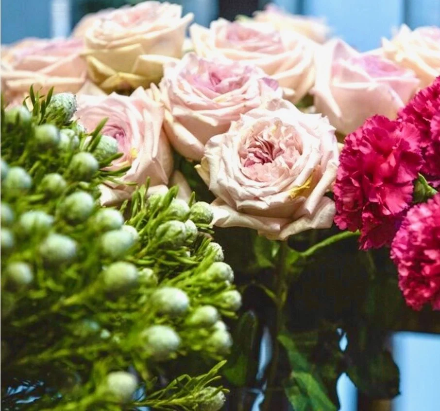 Close-up of pink and white roses and pink carnations among green foliage.