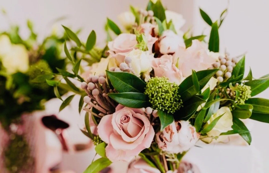 A bouquet of pink and white roses, green berries, and lush green leaves.