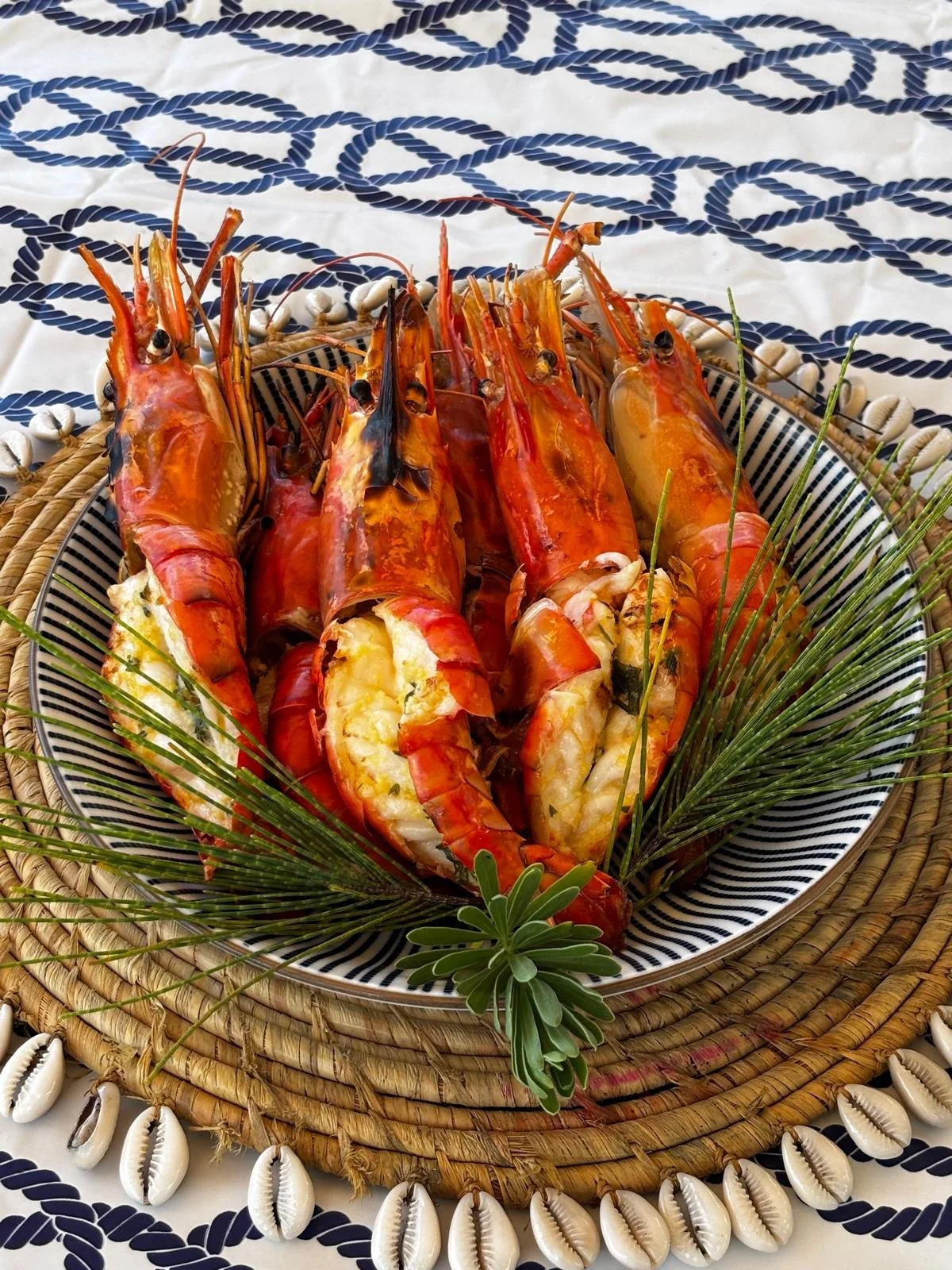Grilled lobster tails served on a decorative plate with green herbs and palm leaves, surrounded by seashells on a woven mat with a patterned tablecloth underneath in Mauritius.