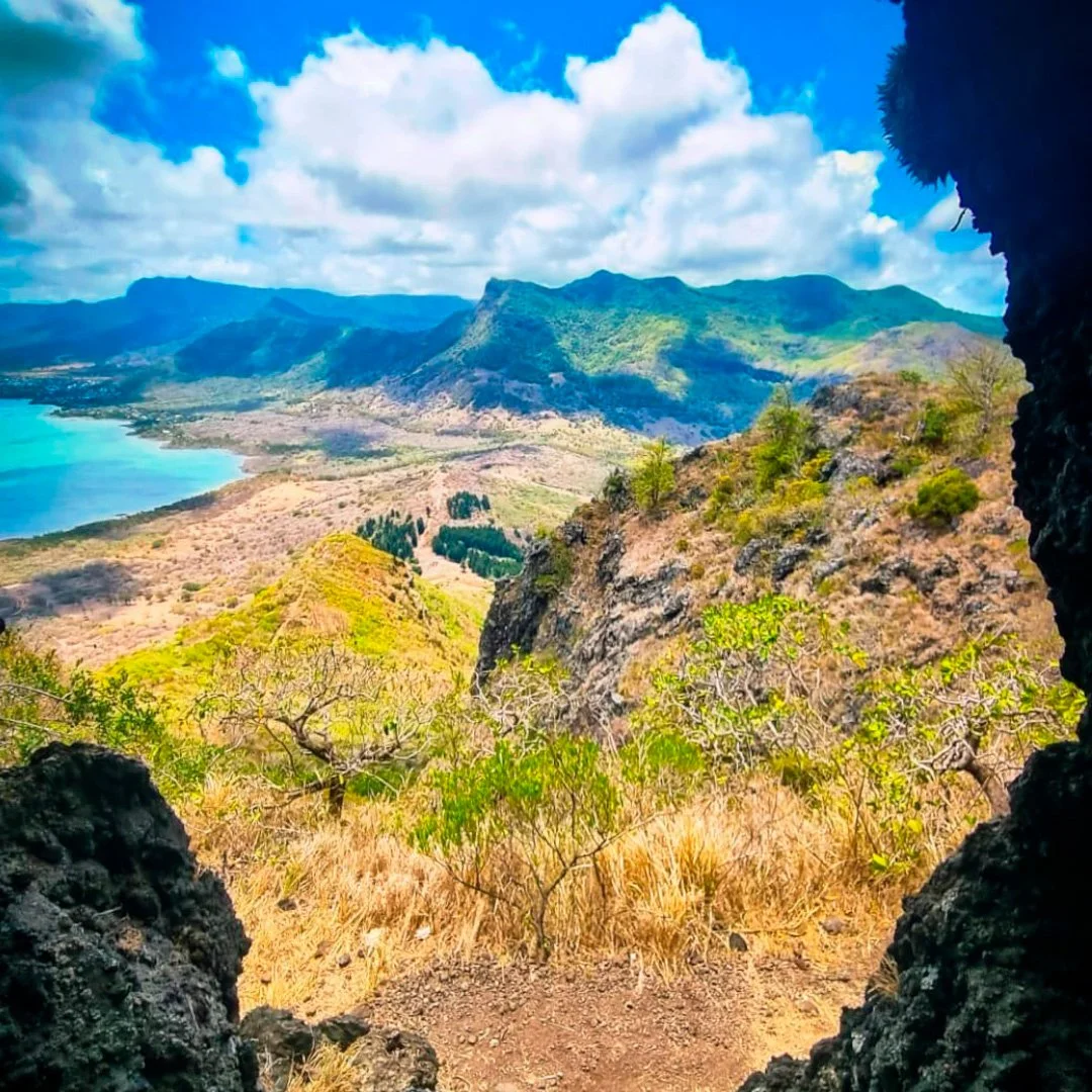 A scenic view of mountains, trees, and a body of water seen from a cave or rocky opening in Mauritius.
