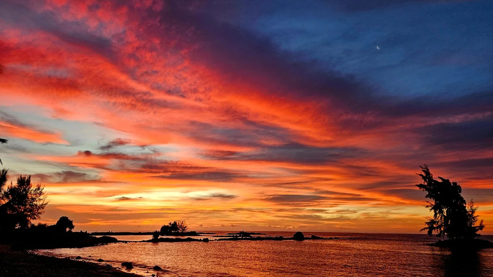 Colorful sunset over a calm body of water with silhouettes of trees and rocks in Mauritius.
