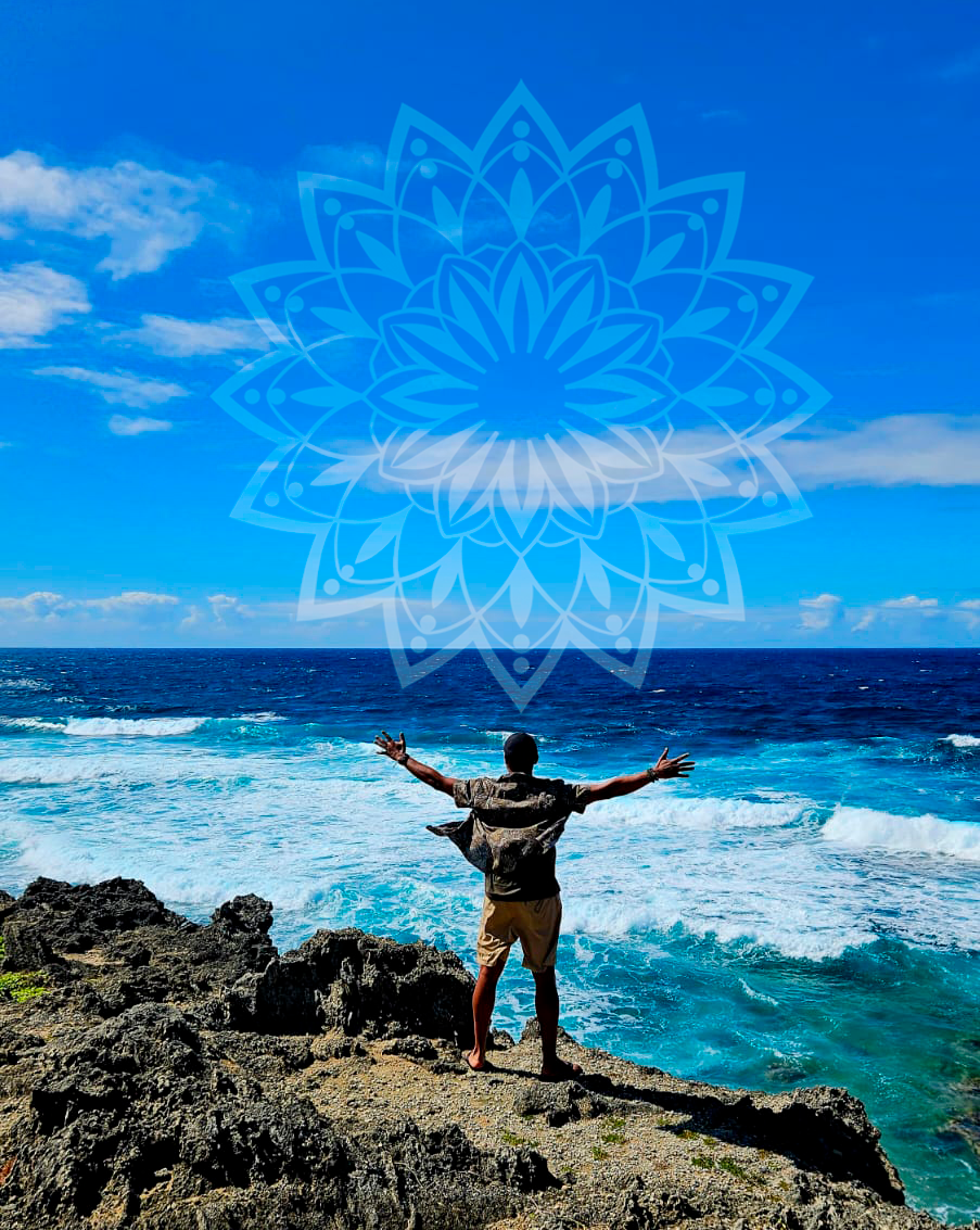 A person standing on rocky coast with arms outstretched, facing the ocean under a partly cloudy sky in Mauritius.