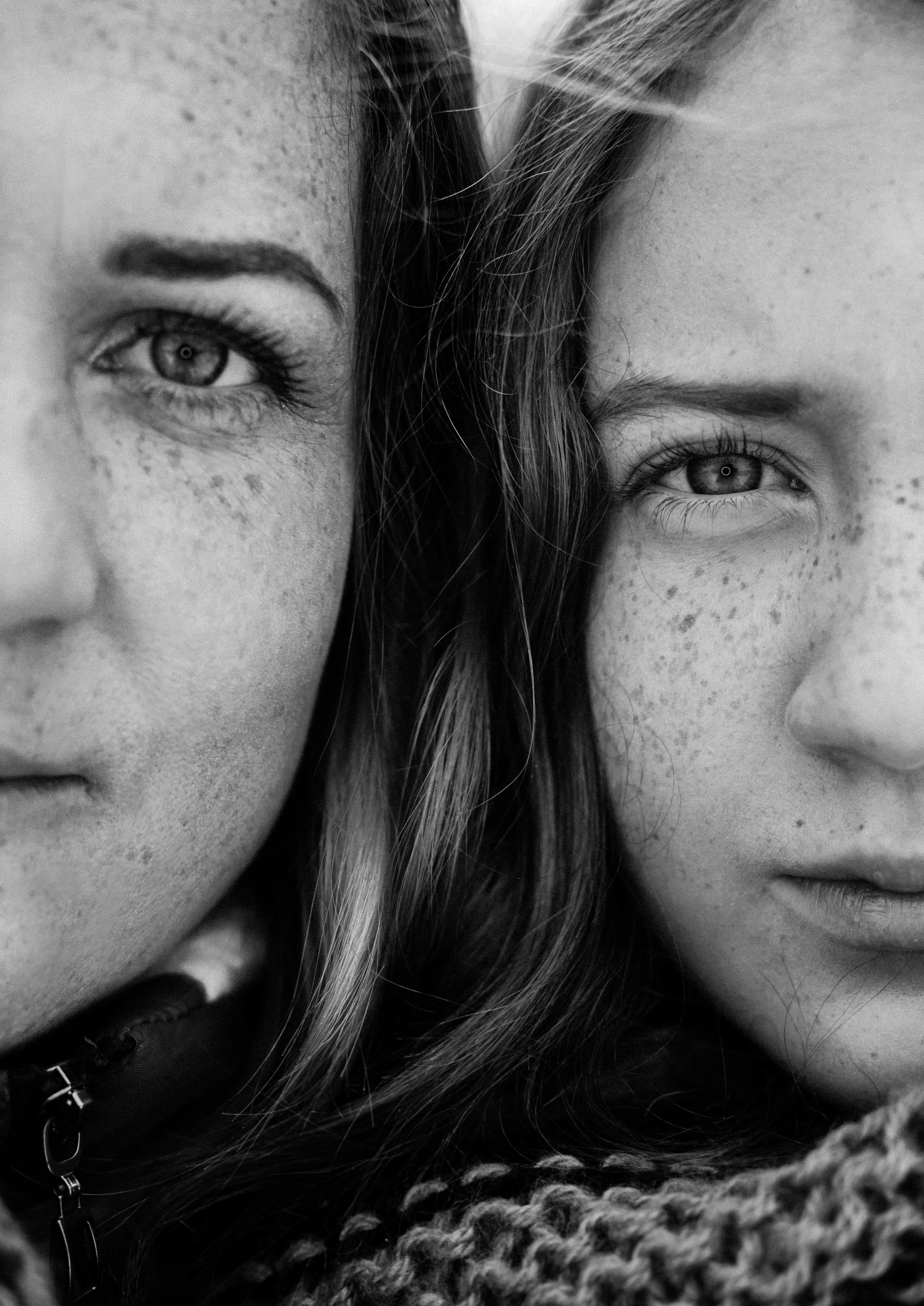 Close-up of two young women with light skin and freckles, one with light-colored hair, both looking directly at the camera in black and white.