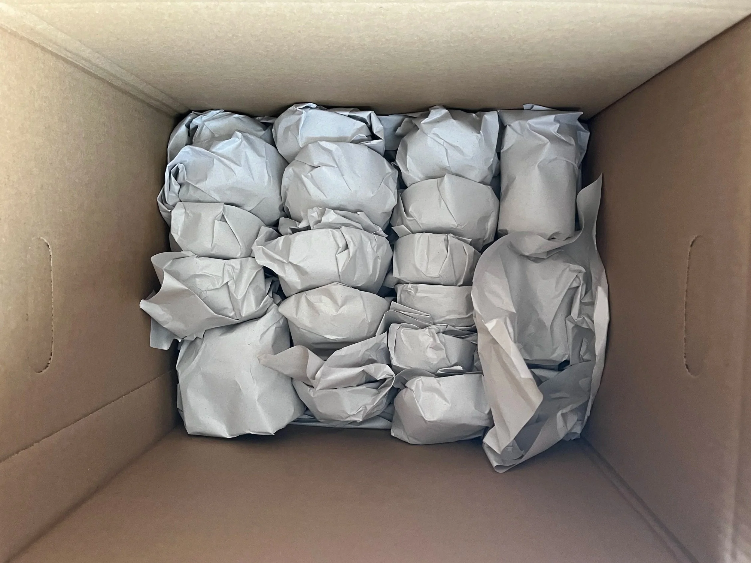 Inside of a cardboard box filled with crumpled white paper used for packing.