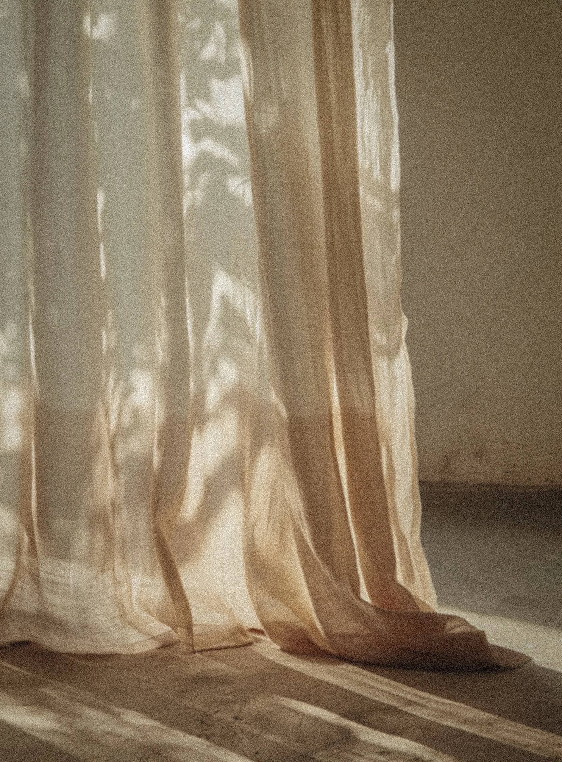 Sunlight filters through beige curtains, casting striped shadows on the wooden floor.