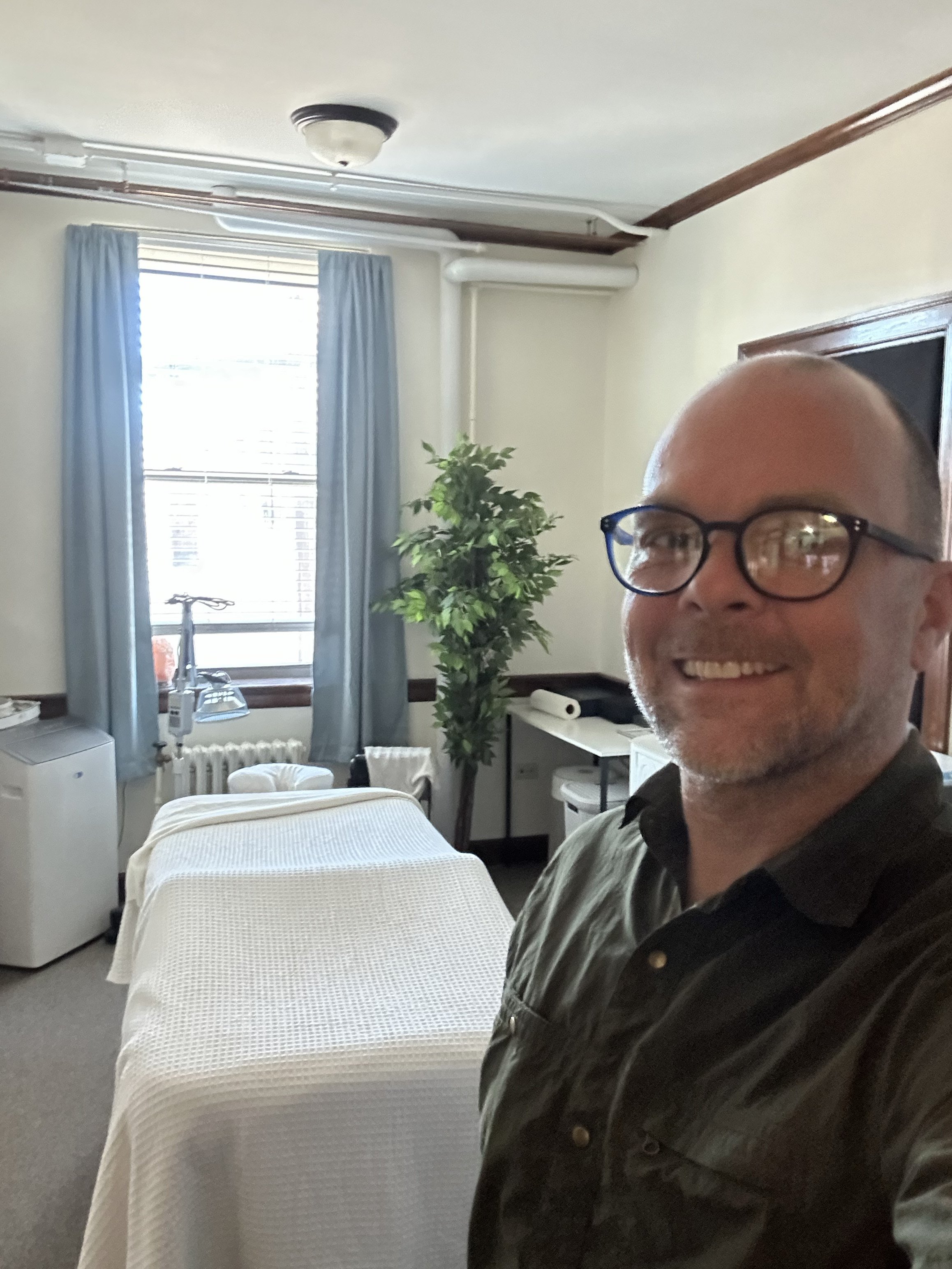 Image of man smiling in his office standing in front of acupuncture equipment