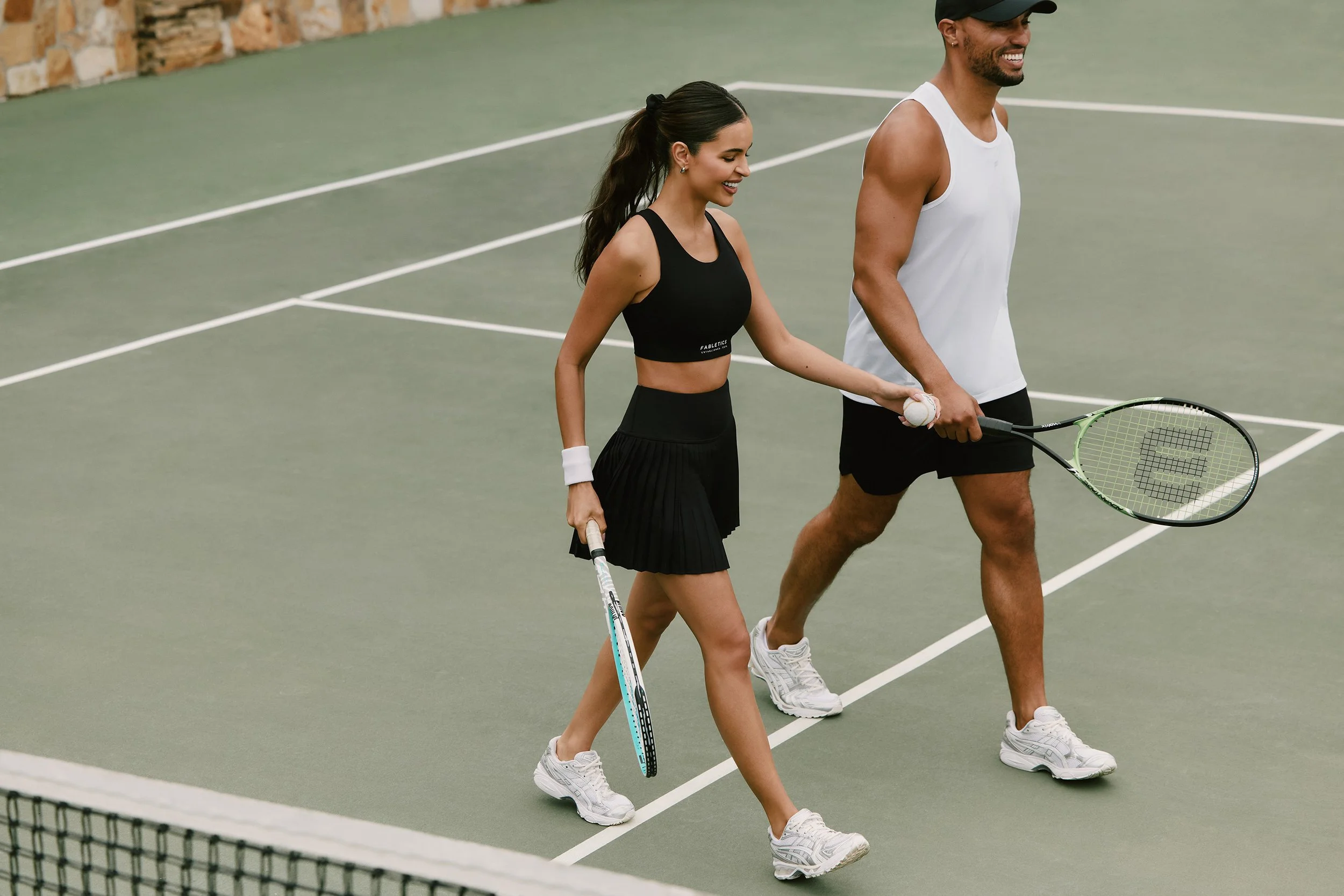 Art director on-figure e-commerce shoot, Los Angeles. A man and a woman walking on a tennis court, each holding a tennis racket, smiling as they walk.