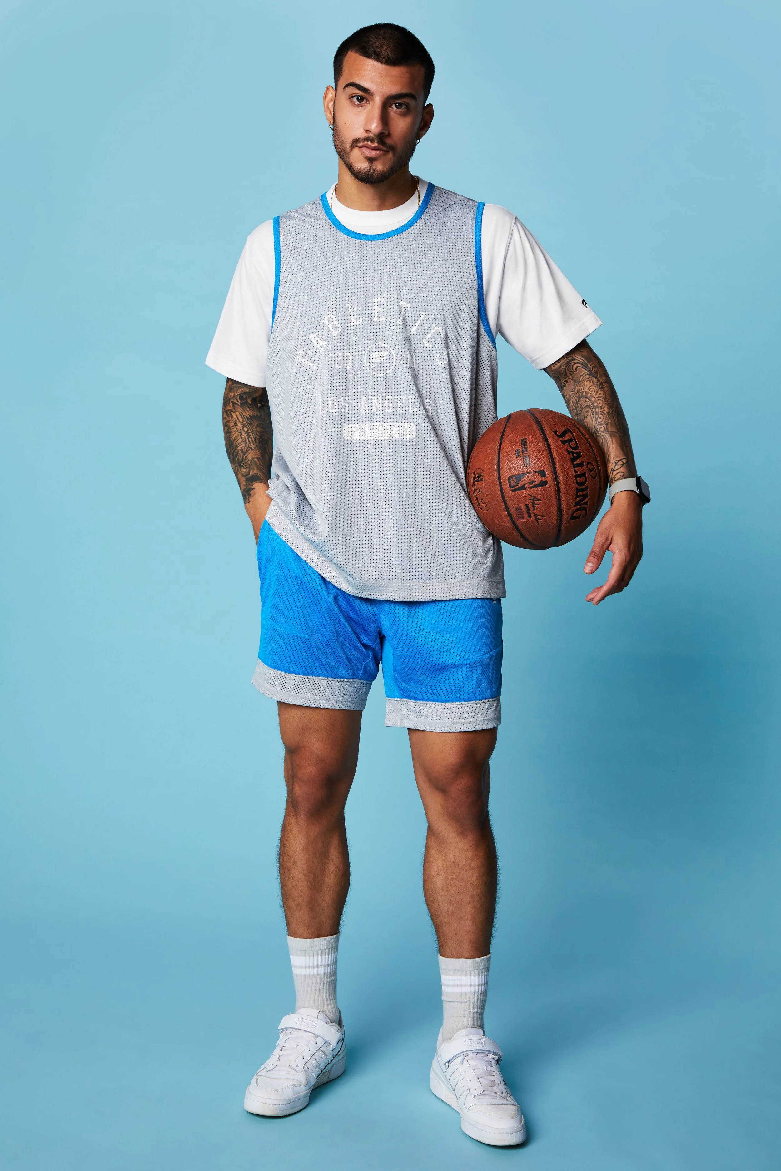 Young man in basketball attire holding a basketball standing against a light blue background.