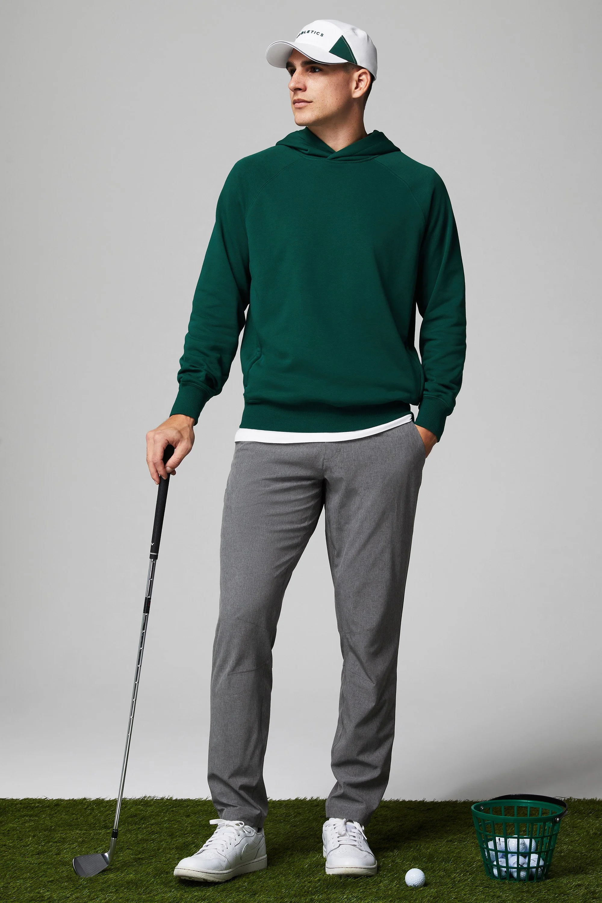 A man standing on artificial grass, holding a golf club, with a golf ball nearby and a basket of golf balls.