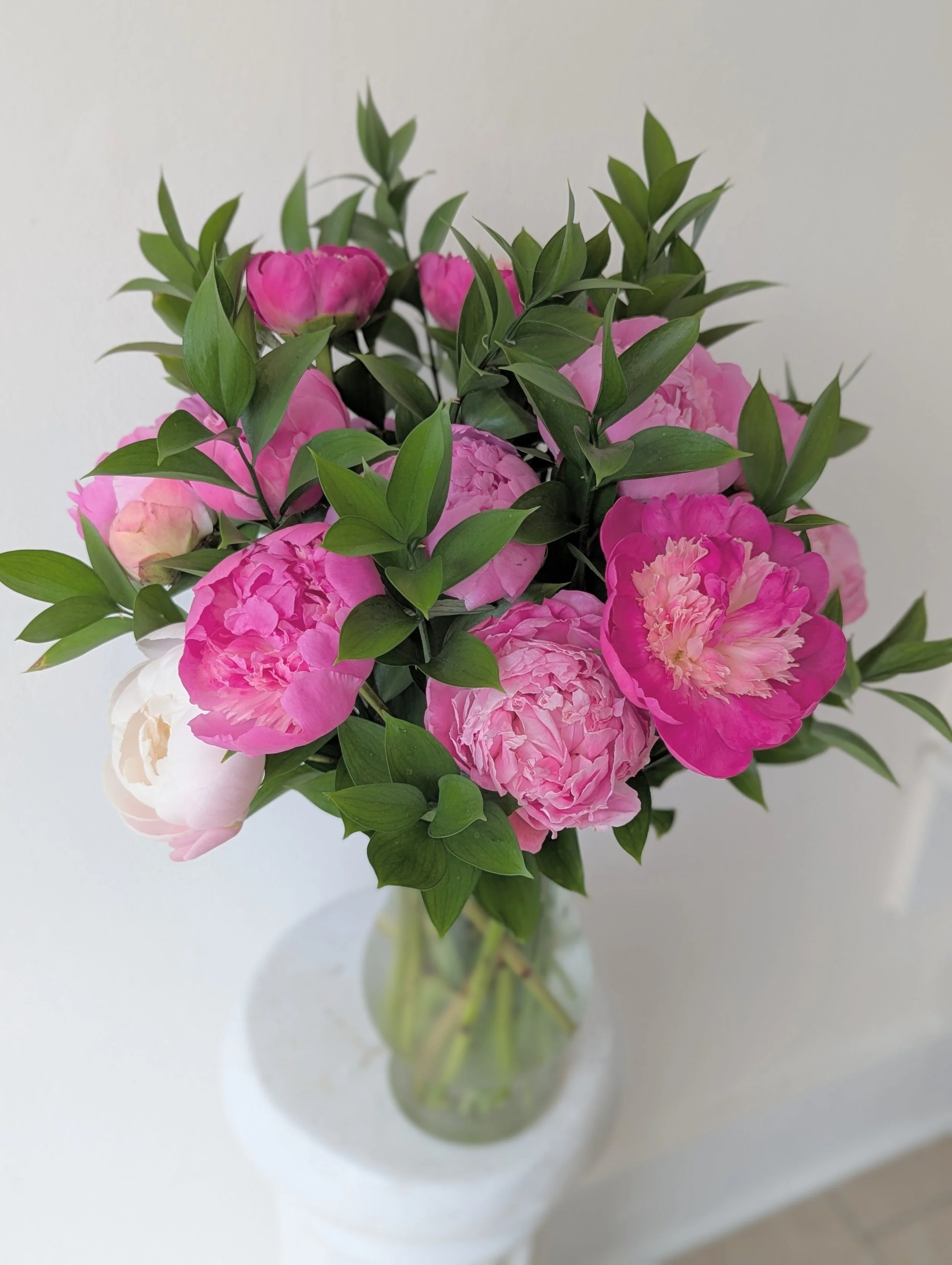 A bouquet of pink peonies with green leaves in a clear glass vase.